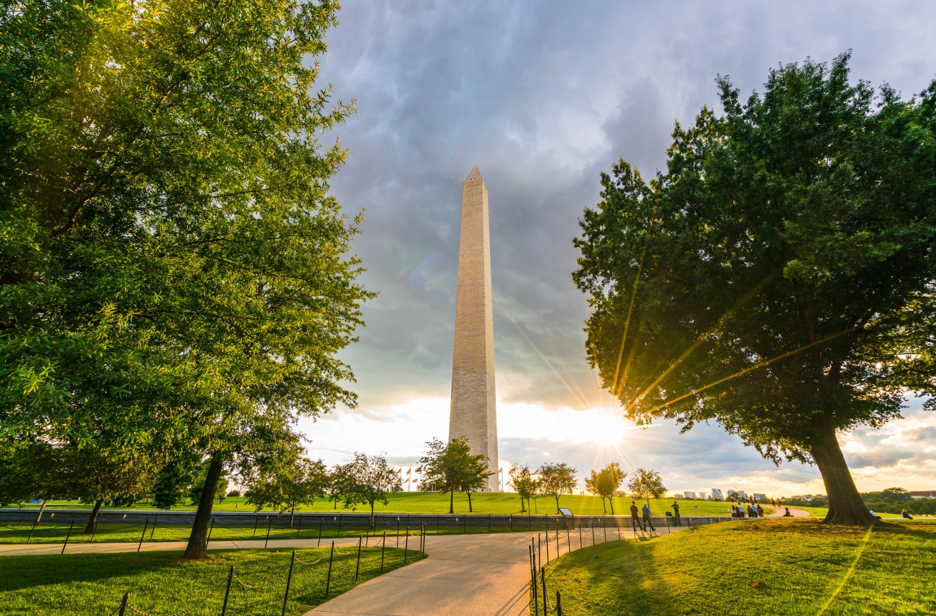 A wide view of the Washington Monument in a park-like setting with trees and a path.