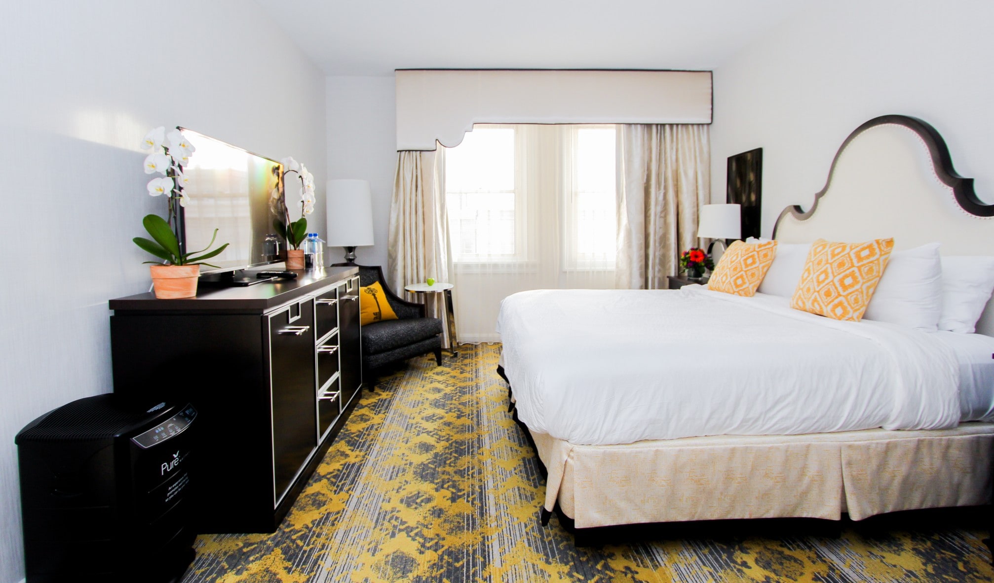 A hotel room with a large bed, dresser, chair, and window