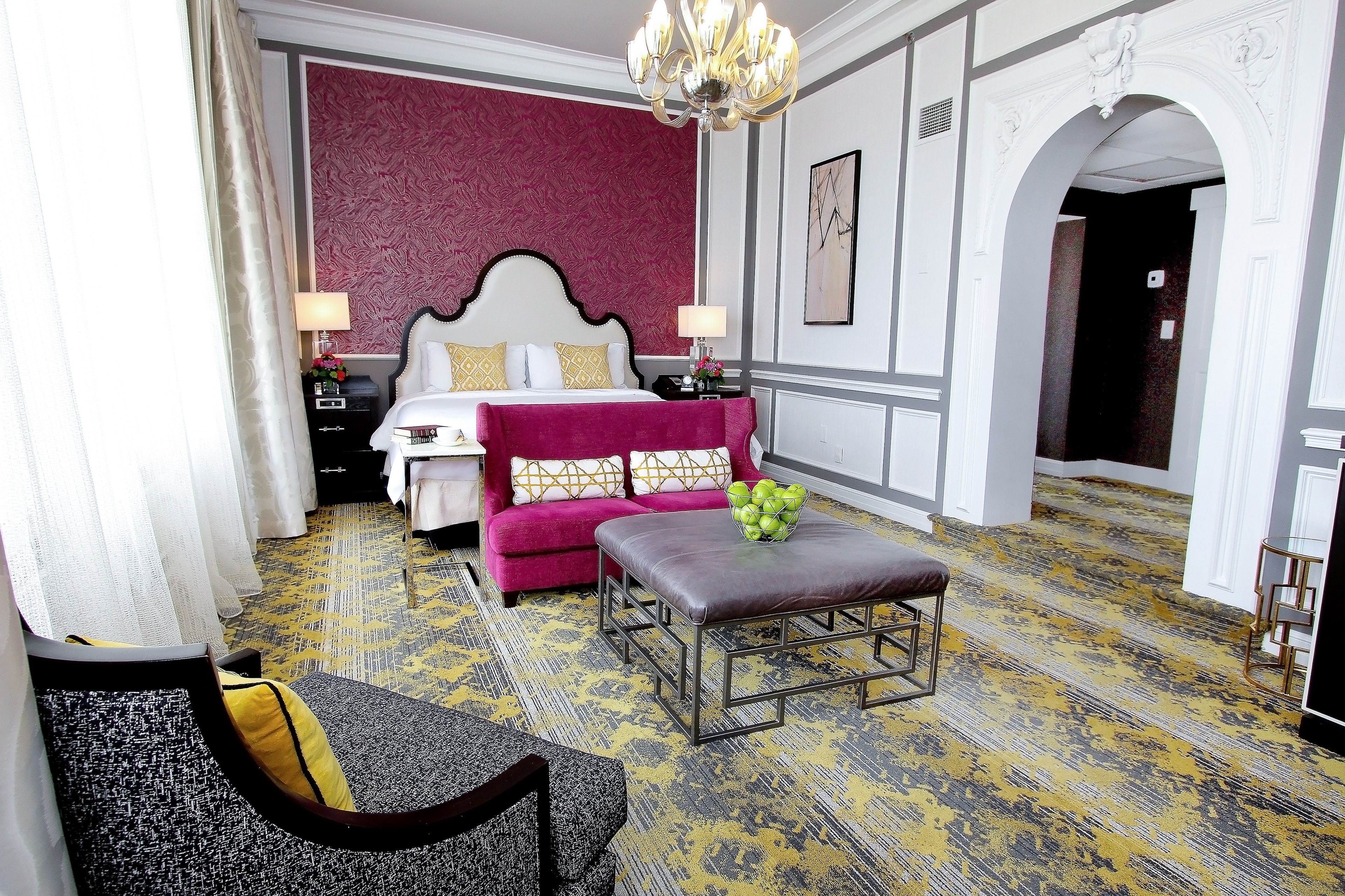 A wide view of a luxurious hotel suite with a king-sized bed, purple sofa, and chandelier.