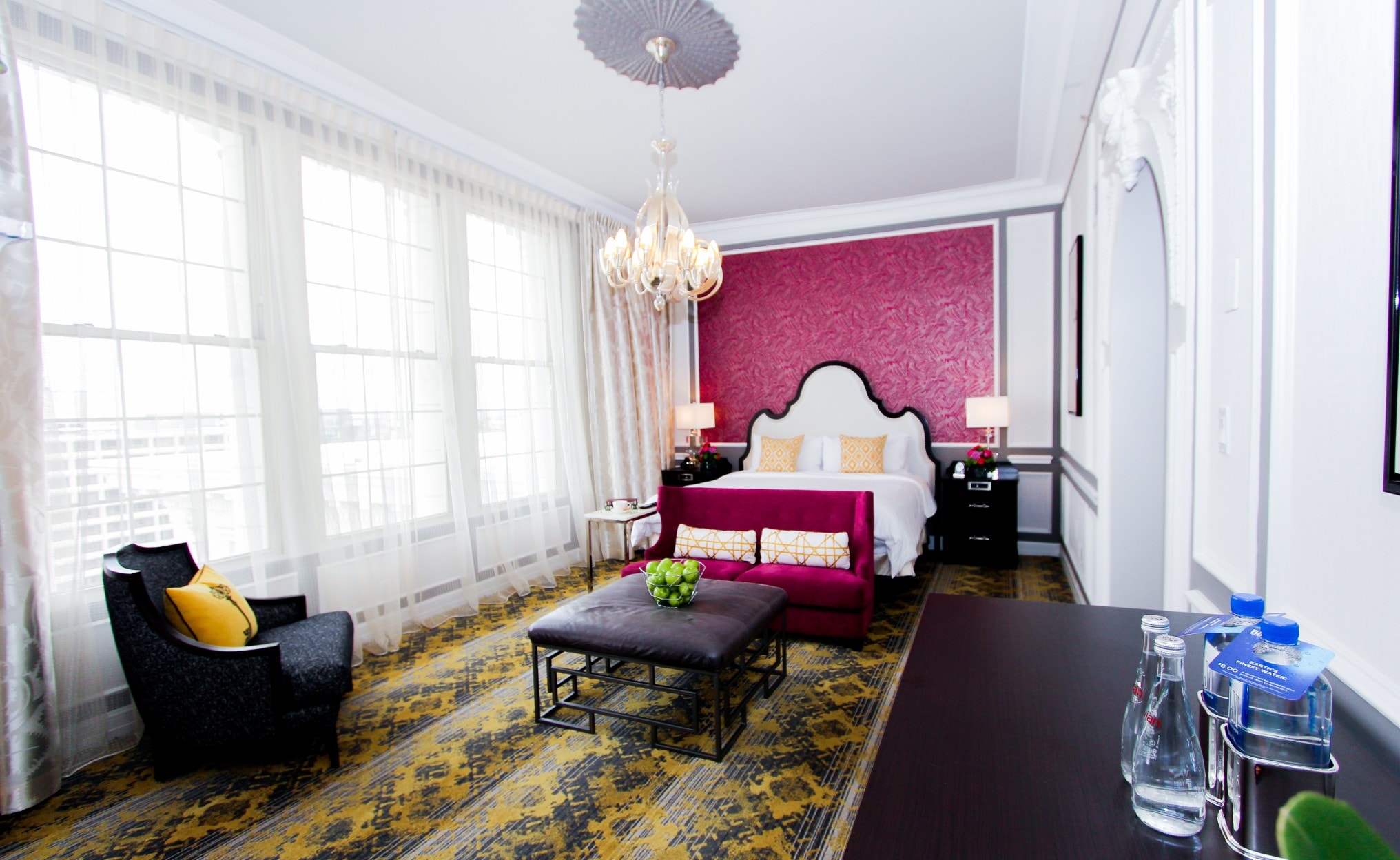 A luxurious hotel room with a large bed, sitting area, and chandelier.