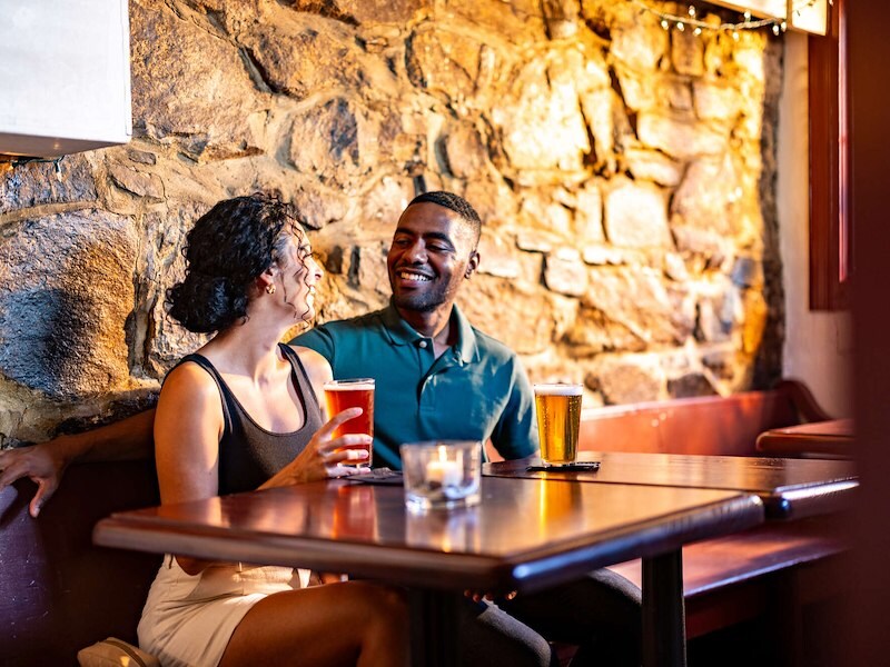 Couple enjoying craft beers at Drummer’s Lot Pub inside Historic Inns of Annapolis’ cozy tavern.