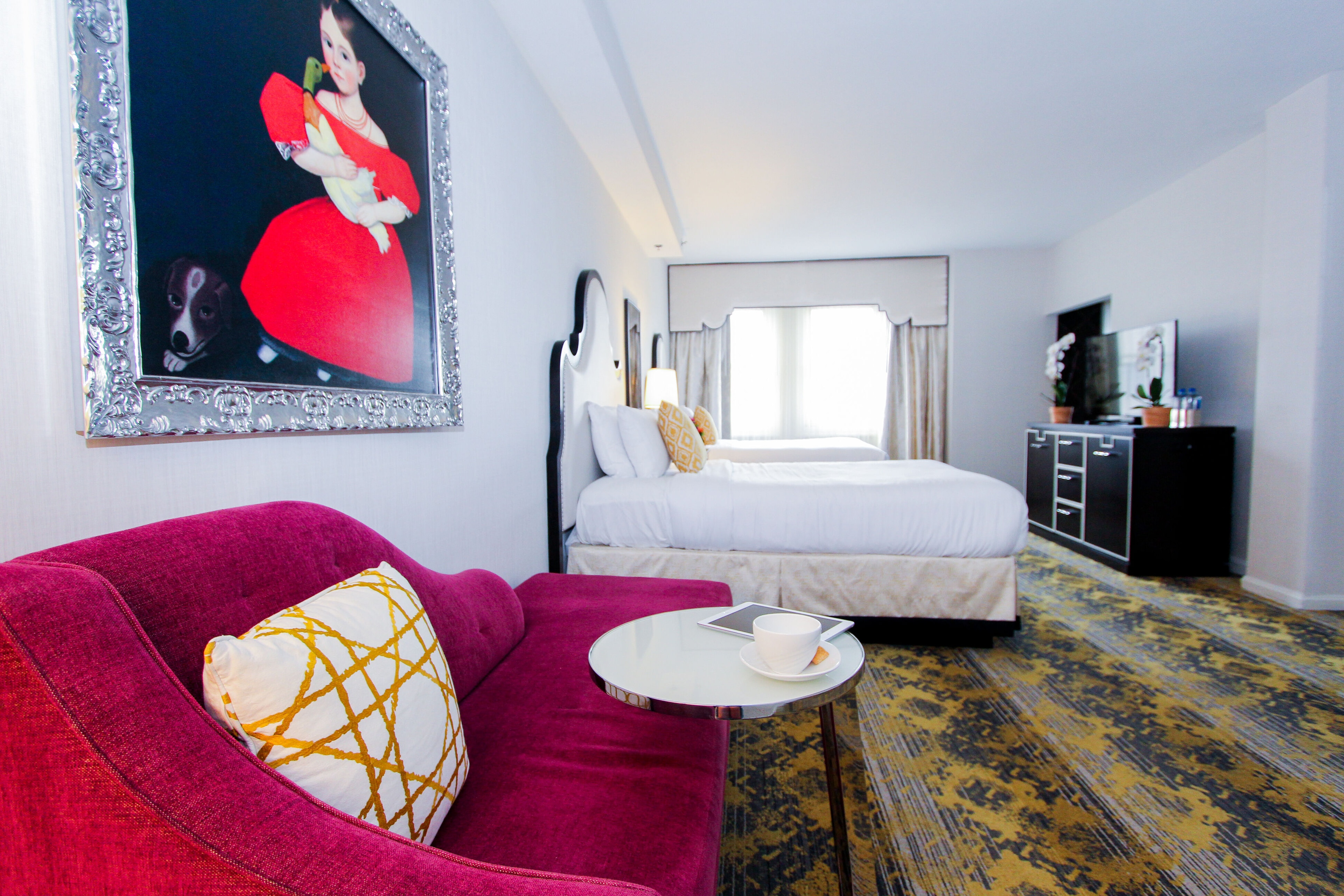 A hotel room with a red sofa, a coffee table, a bed, and a TV stand.