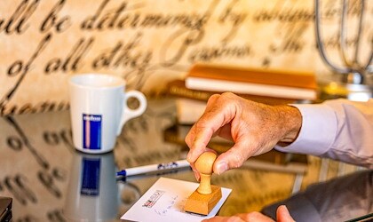 Hand stamping a postcard on a desk with books, pen, and coffee mug at Melrose Georgetown Hotel.