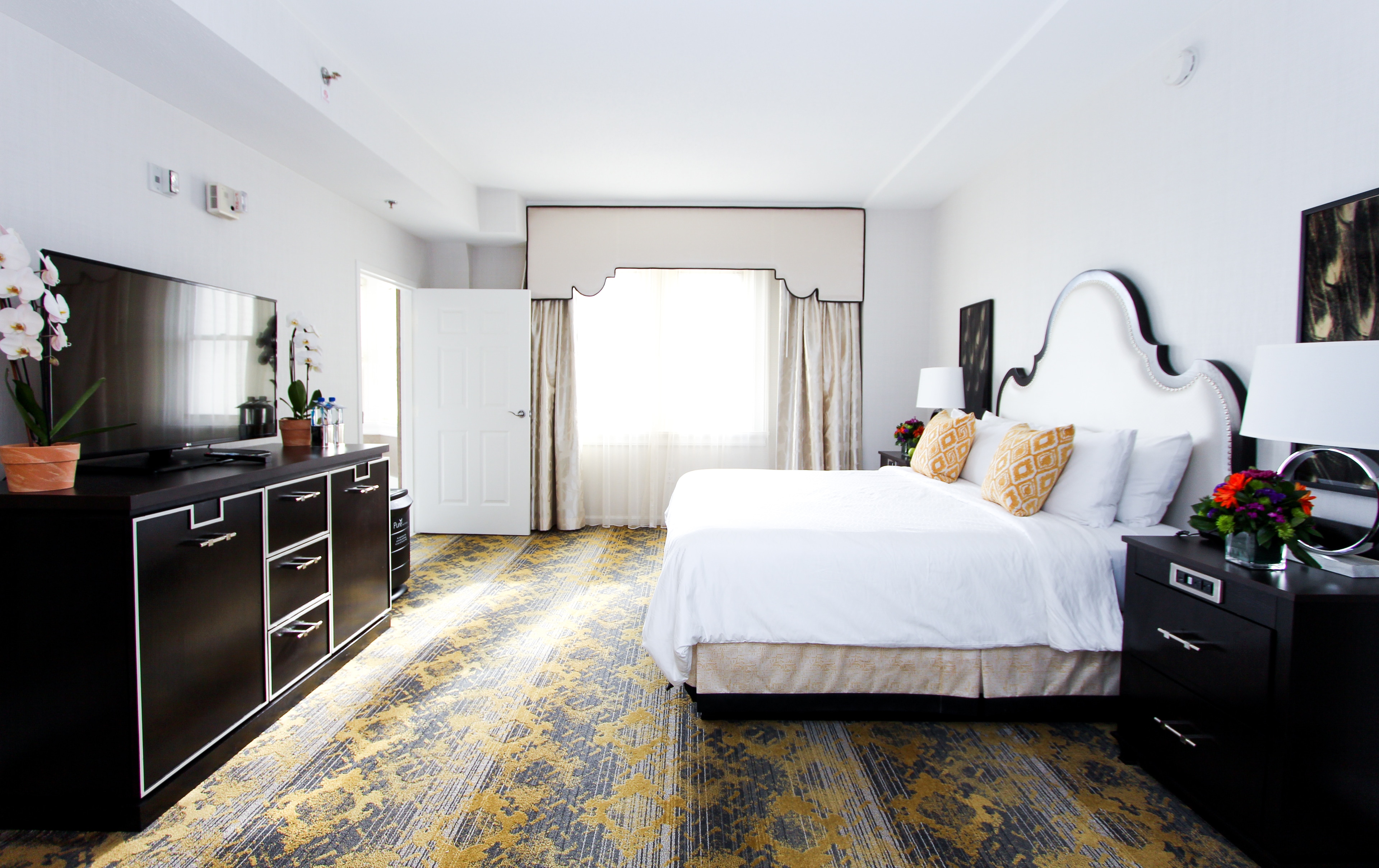 A wide view of a hotel room with a king-sized bed, flat-screen TV, and patterned carpet.