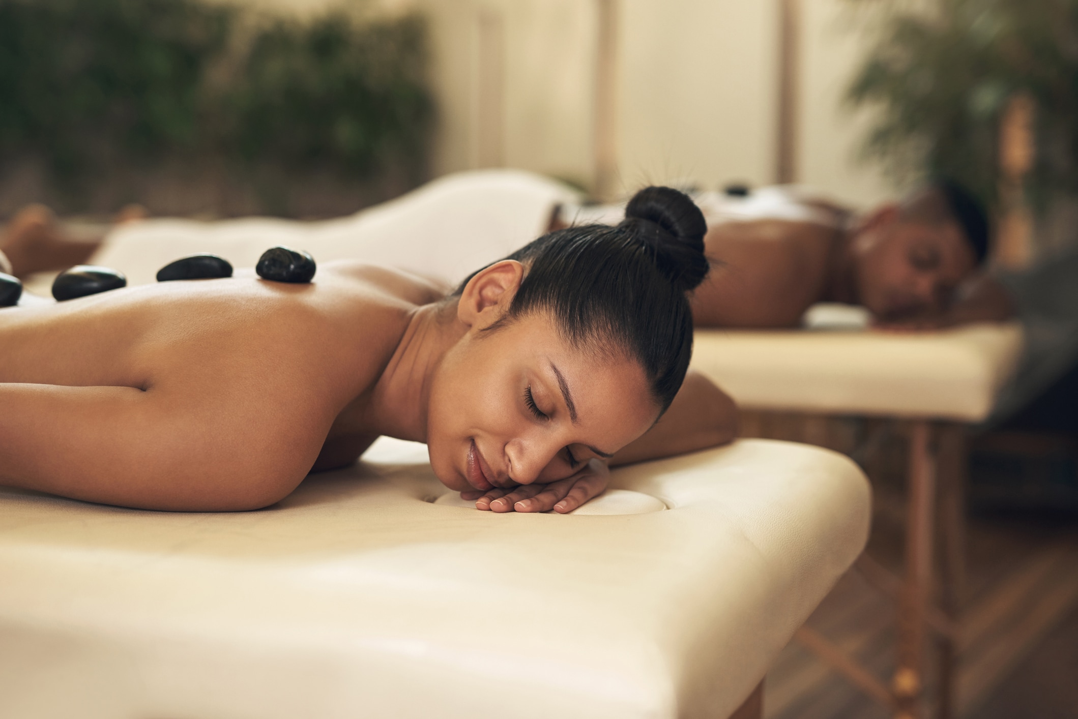 A woman lies on a massage table with hot stones on her back
