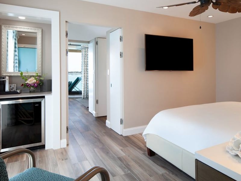 A wide view of a hotel room with a bed, TV, mini fridge, and doorway