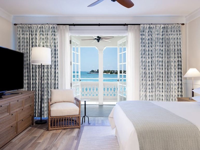 A well-appointed guest room with a large bed, comfortable seating area, and stunning beach view through the balcony doors.