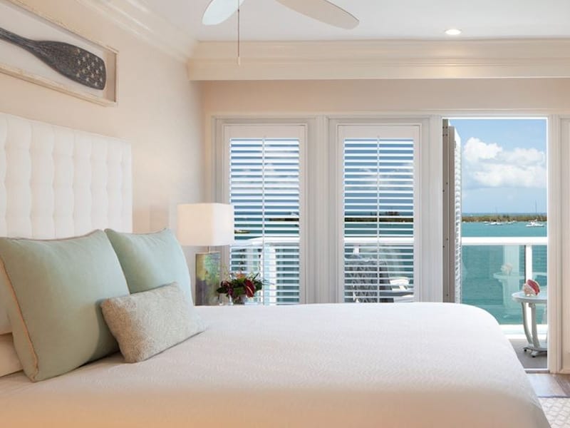 A wide view of a hotel room with a large bed, green pillows, and a balcony with a view of the ocean.
