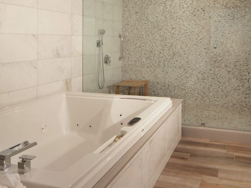 A large white jacuzzi bathtub with a silver faucet and a glass-enclosed shower area with a wooden bench.