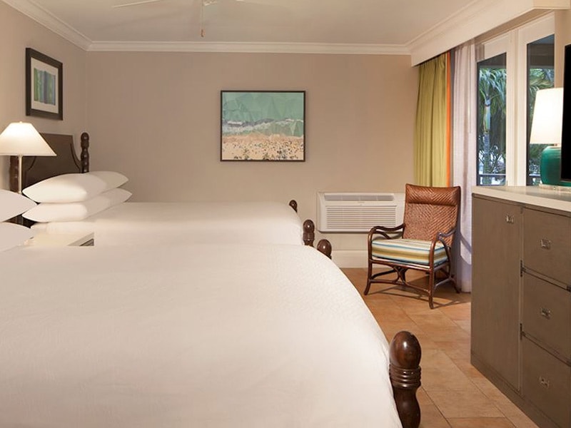 A hotel room with two beds, a dresser, chair, and window