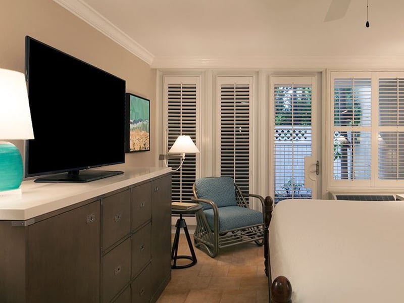 A wide view of a guest room with a TV, chair, lamp, and bed.