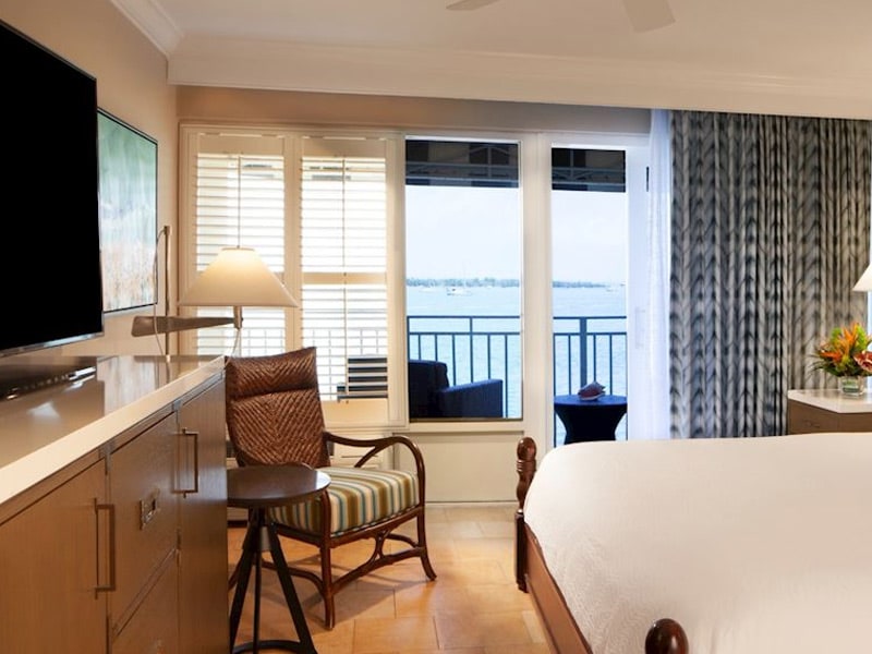 A hotel room with a bed, chair, TV, and balcony with a view.