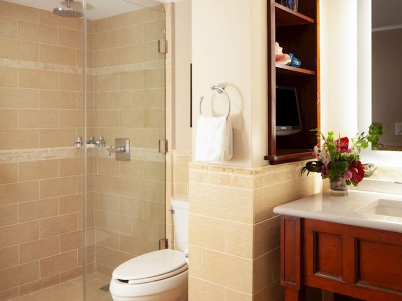 A bathroom with a glass-enclosed shower, toilet, and a sink with a vase of flowers.