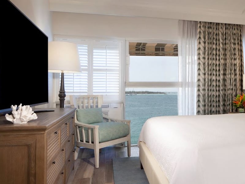 A wide view of a guest room with a bed, chair, TV, and ocean view.