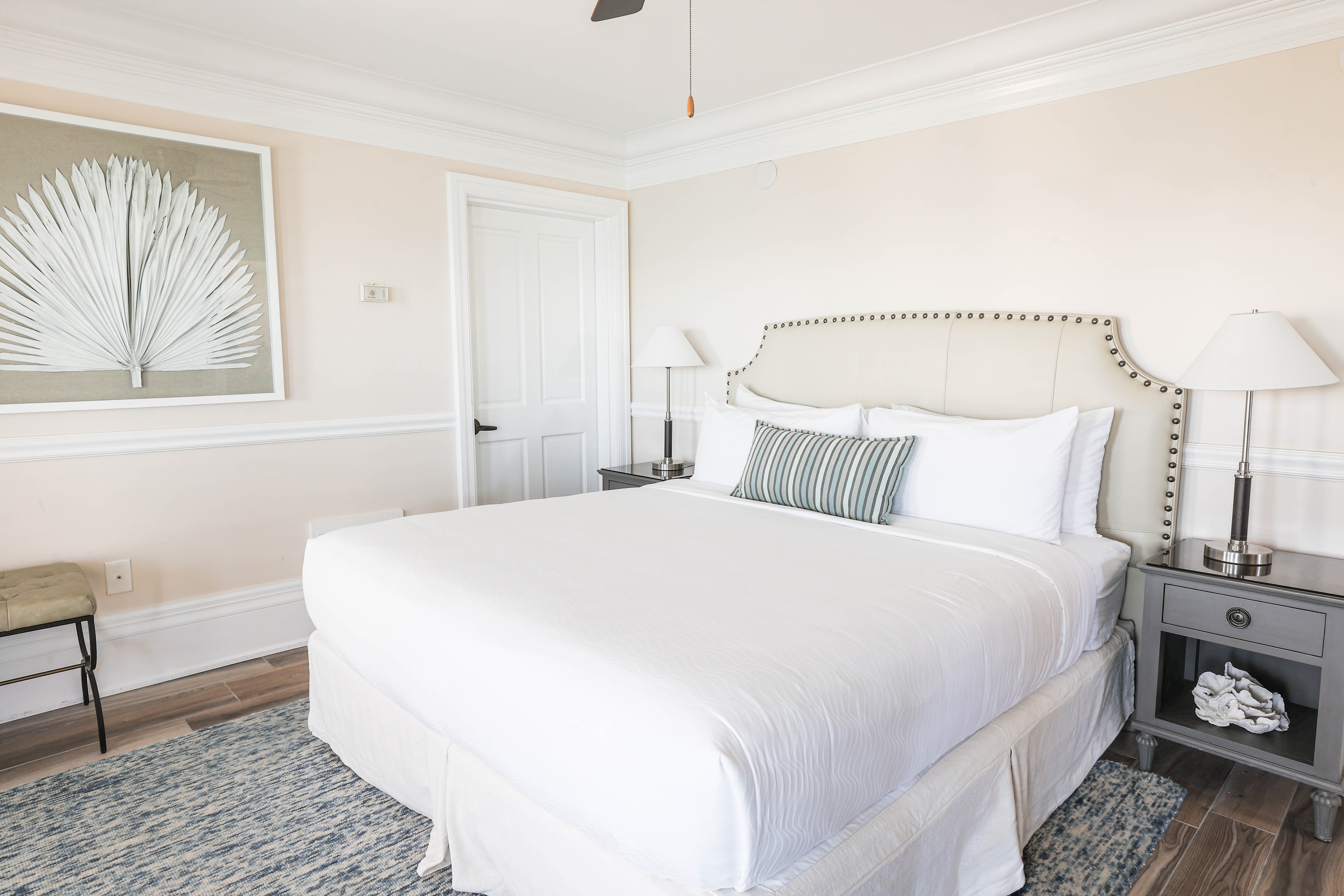 A neatly made bed with white bedding and blue accent pillows in a room with beige walls and a blue rug.