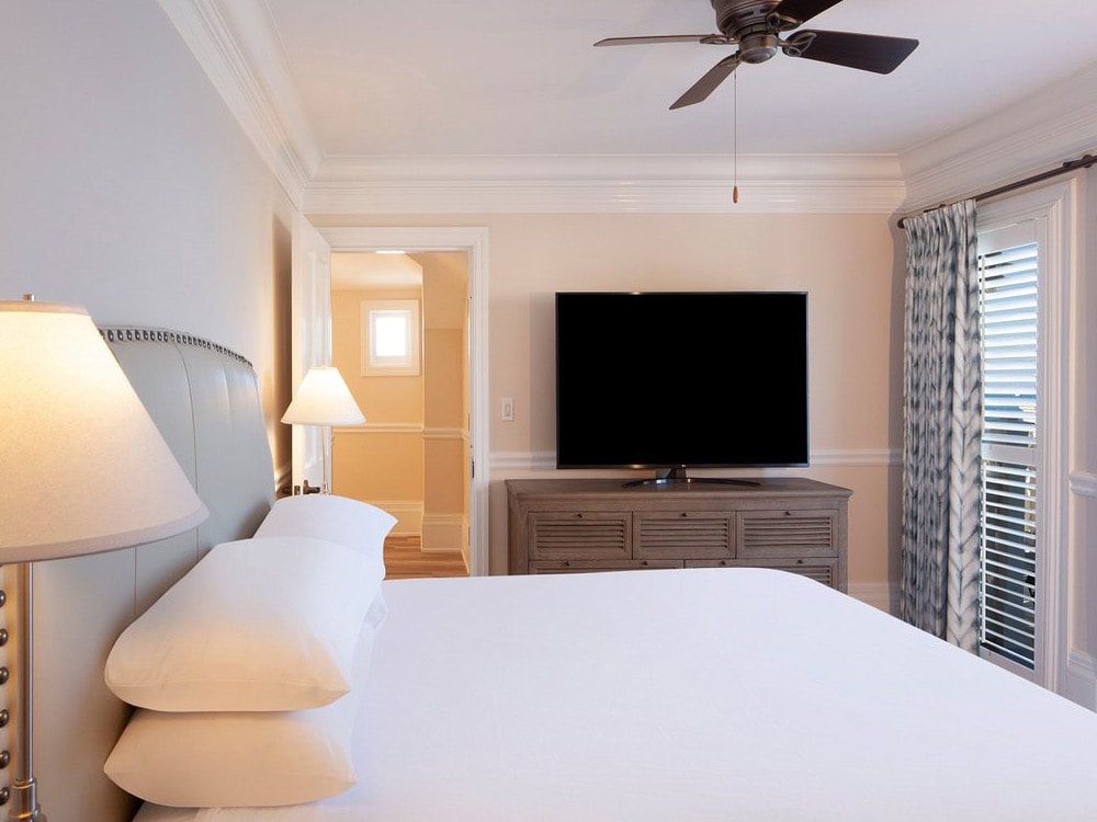 A wide view of a guest room with a large bed, flat-screen TV, and window with blinds.