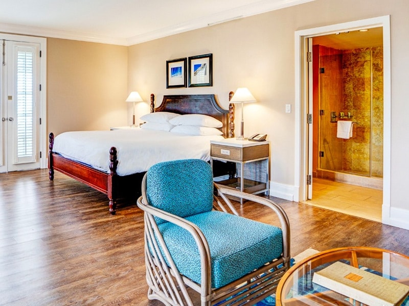A wide view of a hotel room with a large bed, blue accent chair, and open doorway to the bathroom.