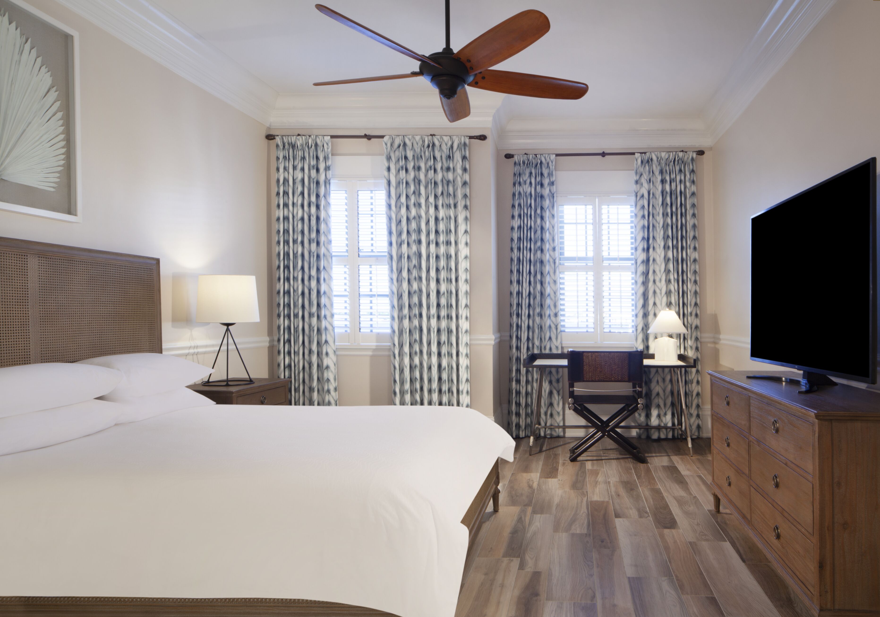 A hotel room with a bed, desk, TV, and window