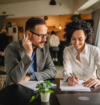 A man and woman are sitting at a table with papers and a laptop