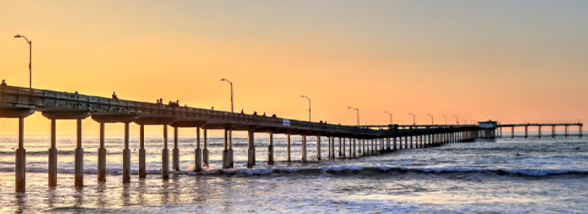 Beautiful beach at sunset with golden light reflecting on the ocean, a long pier stretching into the horizon