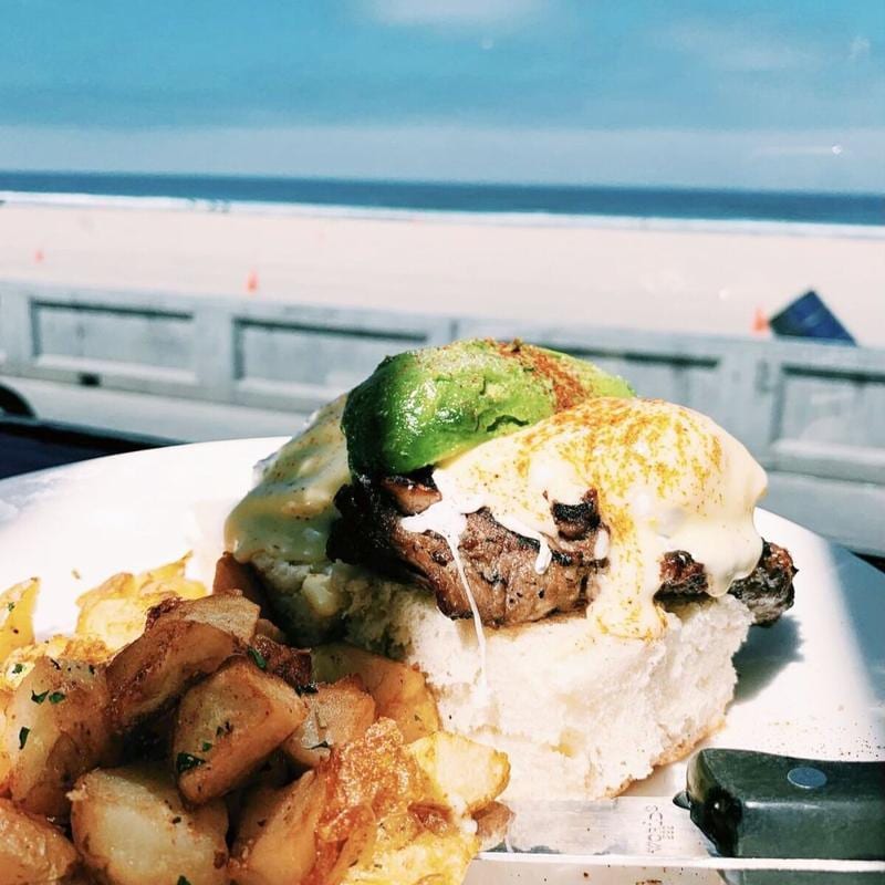 a plate of food with a burger and potatoes in front of a beach