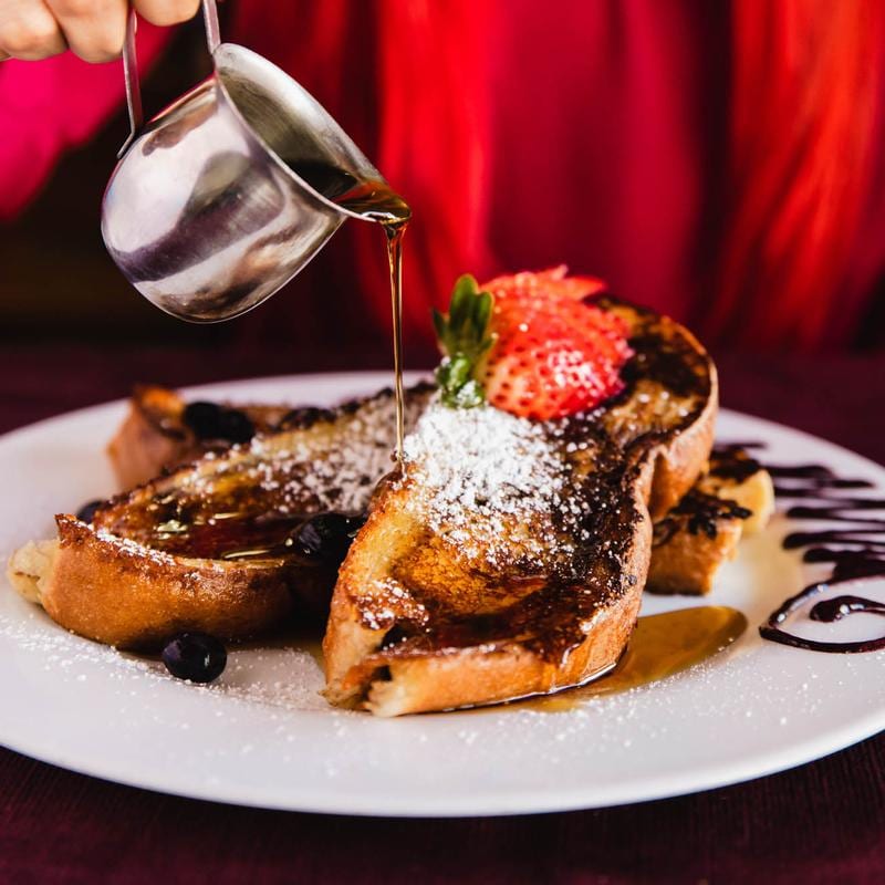 A plate of French toast with strawberries, syrup, and powdered sugar