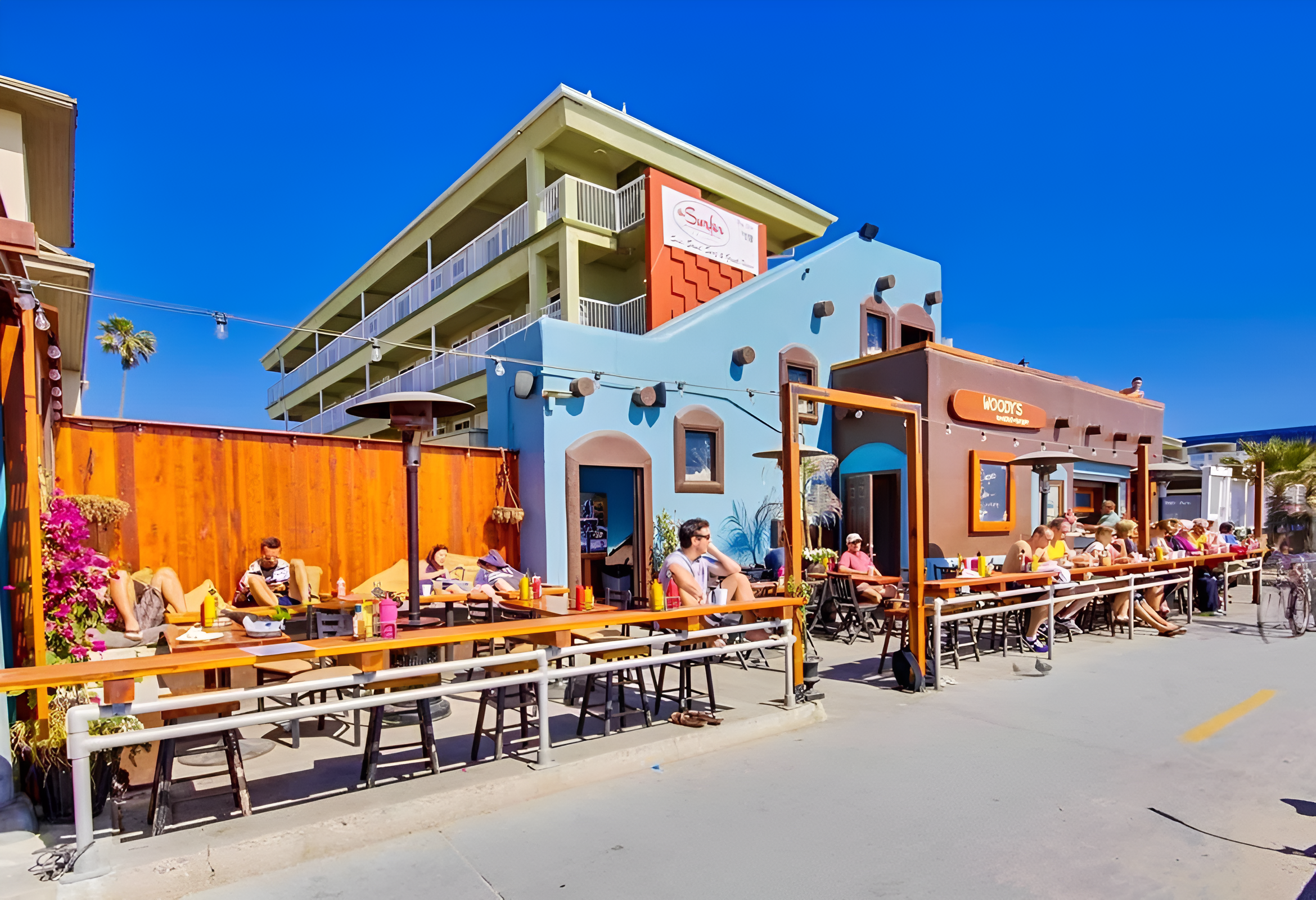 A patio dining area with people sitting at tables outside a restaurant and bar.