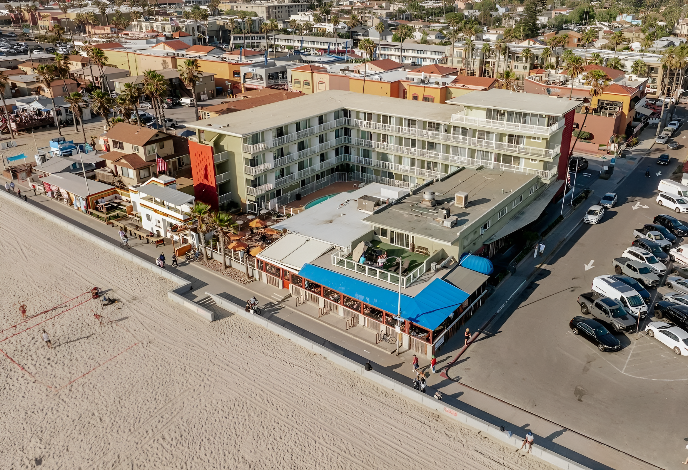 Aerial view of a multi-story hotel with a pool and beach access.