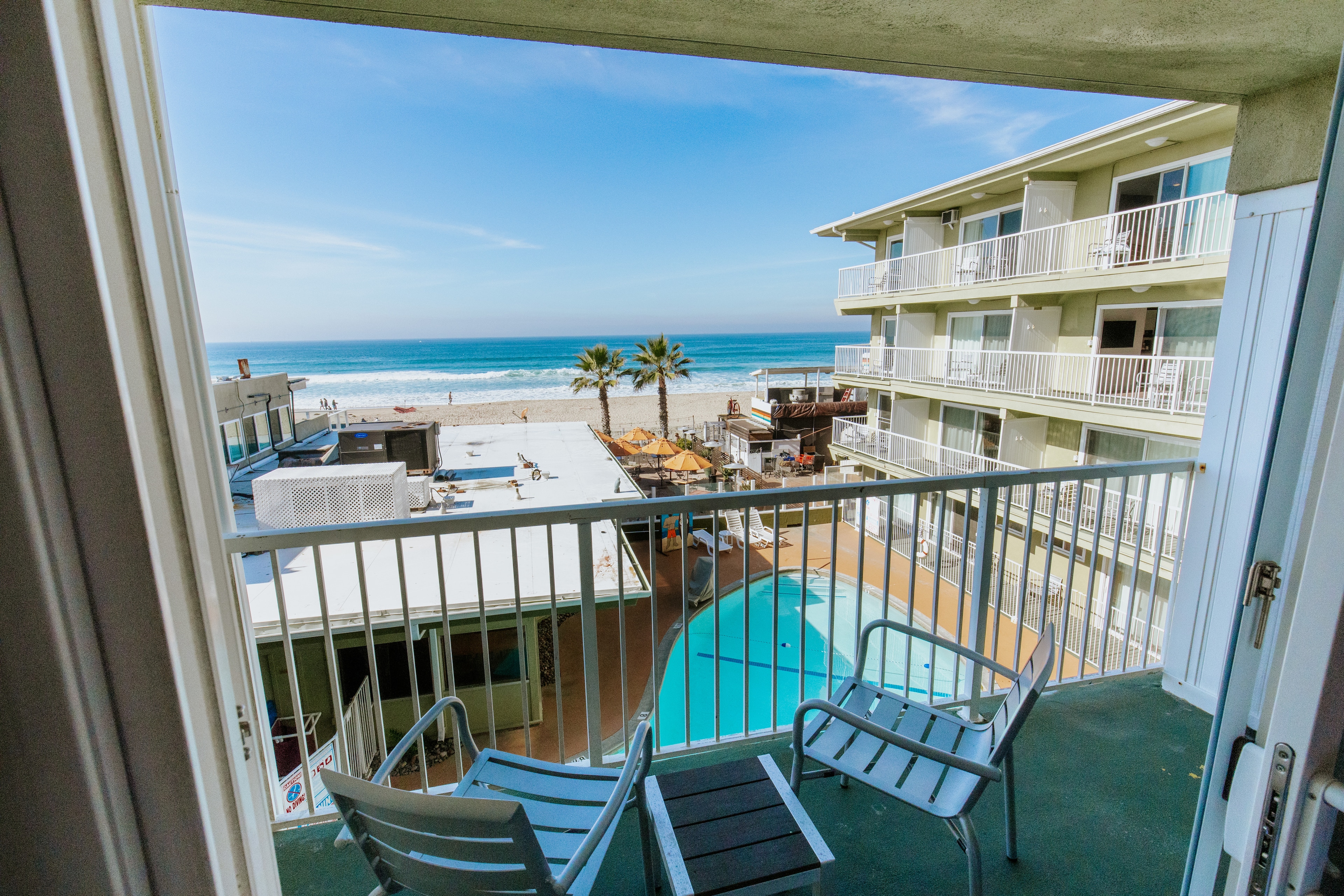 A balcony with a view of the ocean, pool, and beach