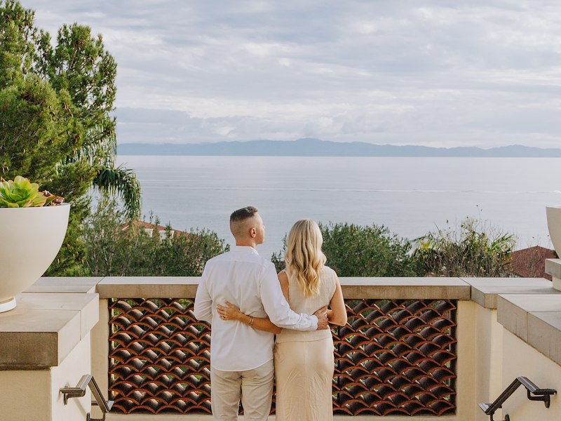 A man and woman standing on a balcony overlooking the ocean