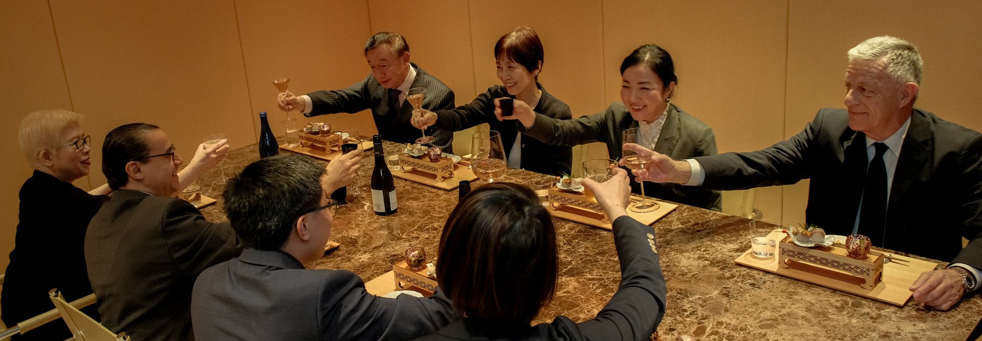 A group of people in business suits sitting at a table toasting, Kitano Hotel New York