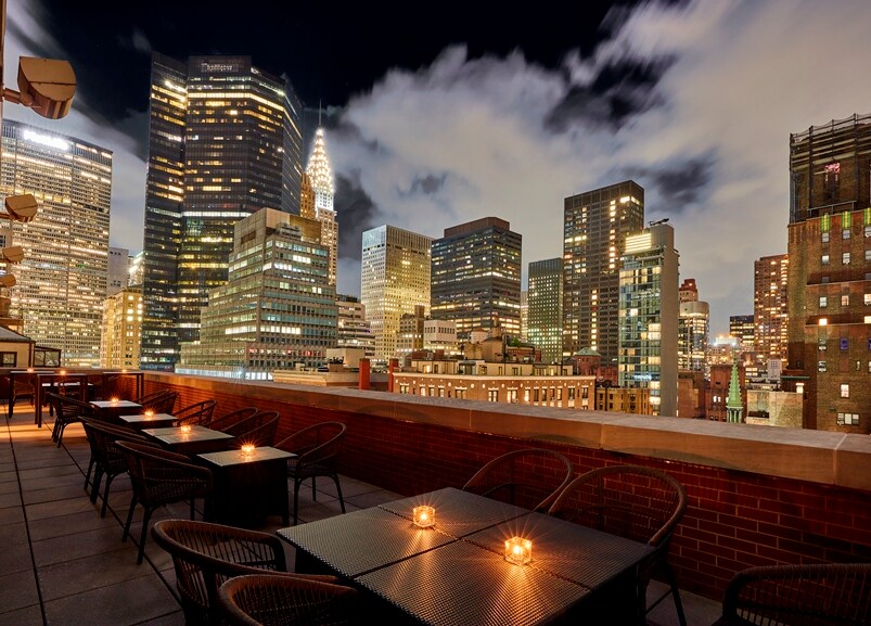 A rooftop terrace with tables and chairs overlooking the city skyline, The Kitano Hotel New York