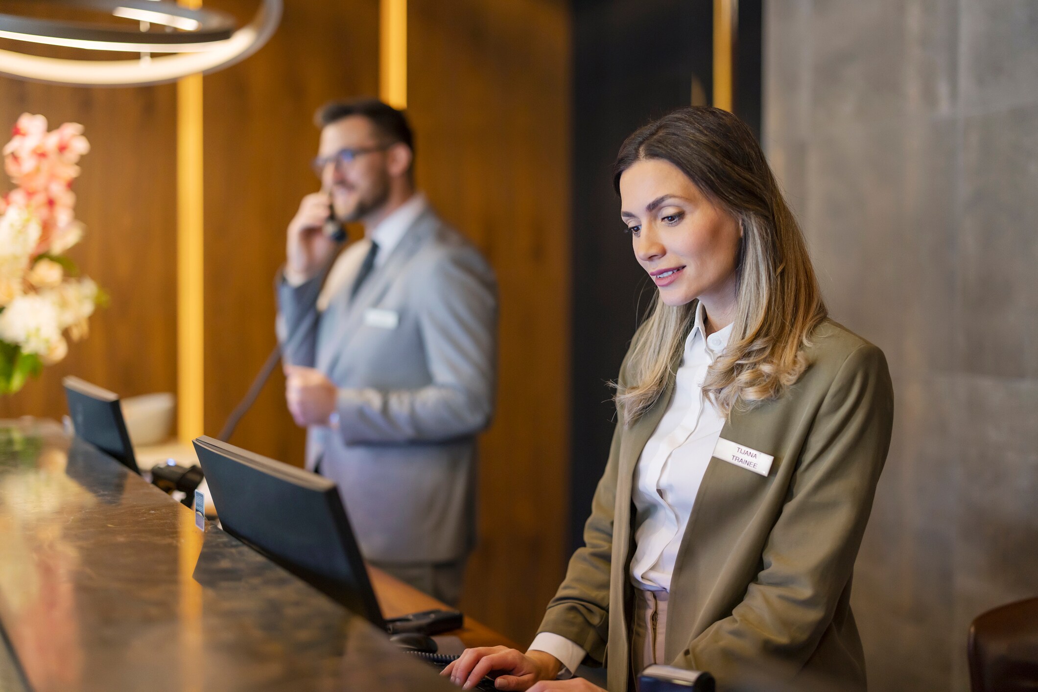 Hotel front desk with a female receptionist assisting guests and a male staff member on the phone - The Otesaga Resort Hotel, New York