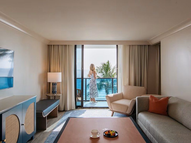 A woman standing on a balcony looking out to a room with a couch and a table
