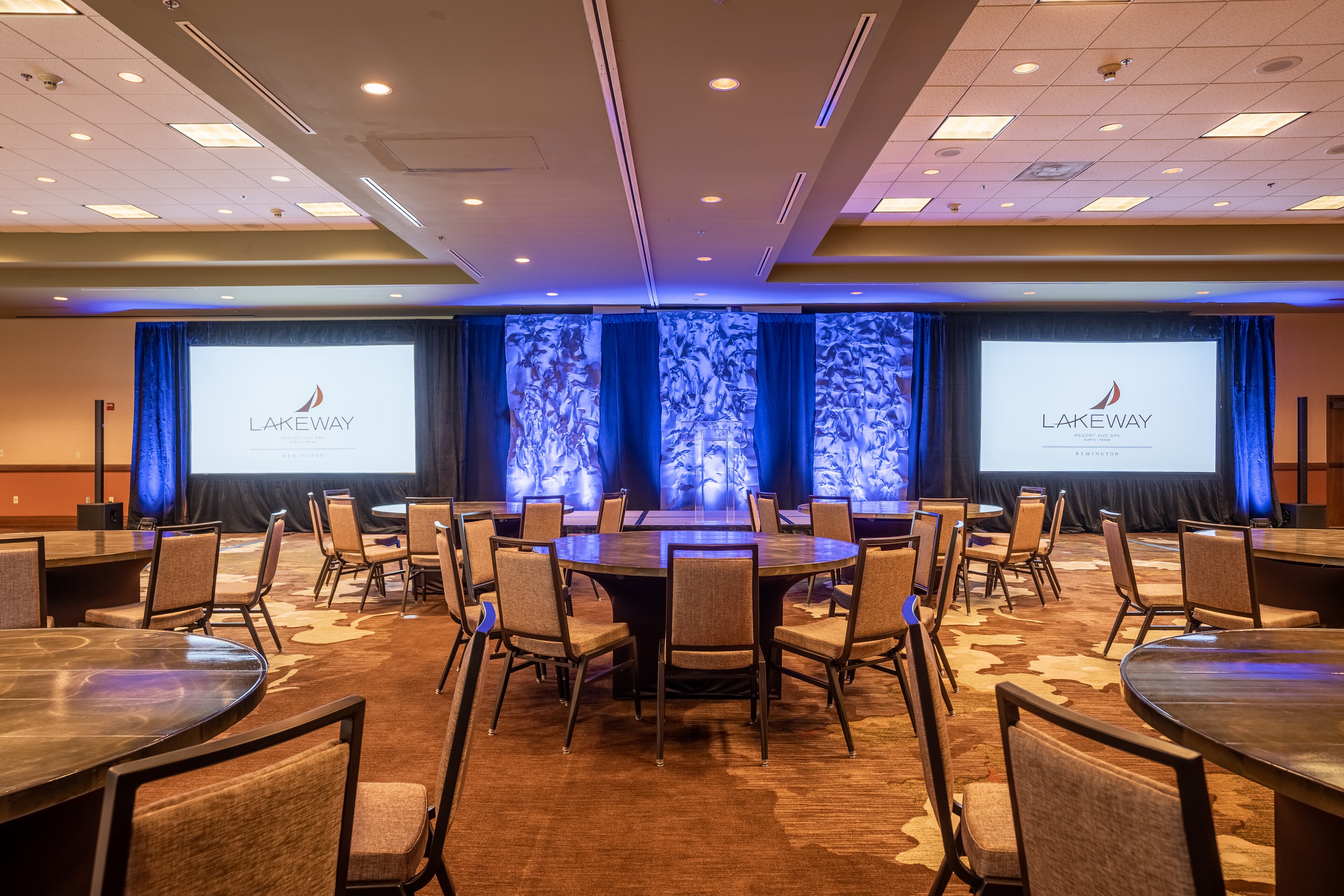 Conference room setup with round tables, stage, and dual screens at Lakeway Resort & Spa, Texas