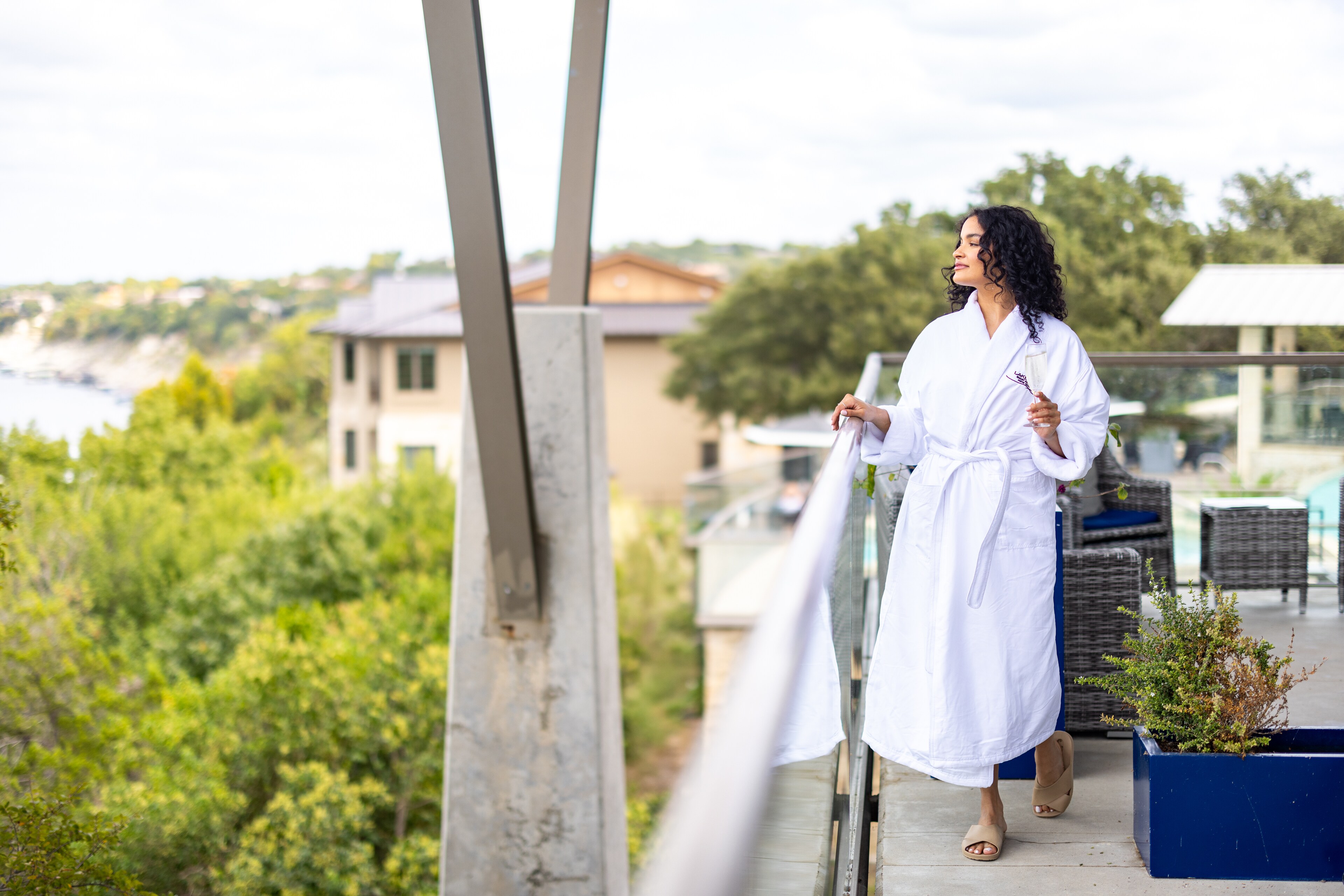 Woman in a white robe standing on a balcony, holding a drink at Lakeway Resort & Spa, Texas