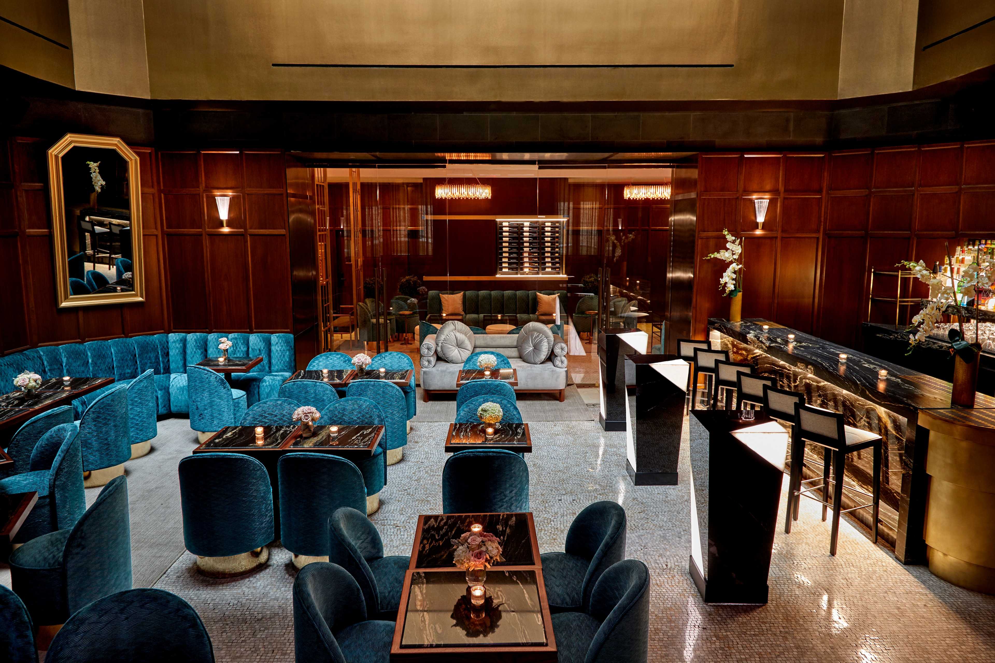 A luxurious lounge with teal chairs, wood paneling, and a marble floor.