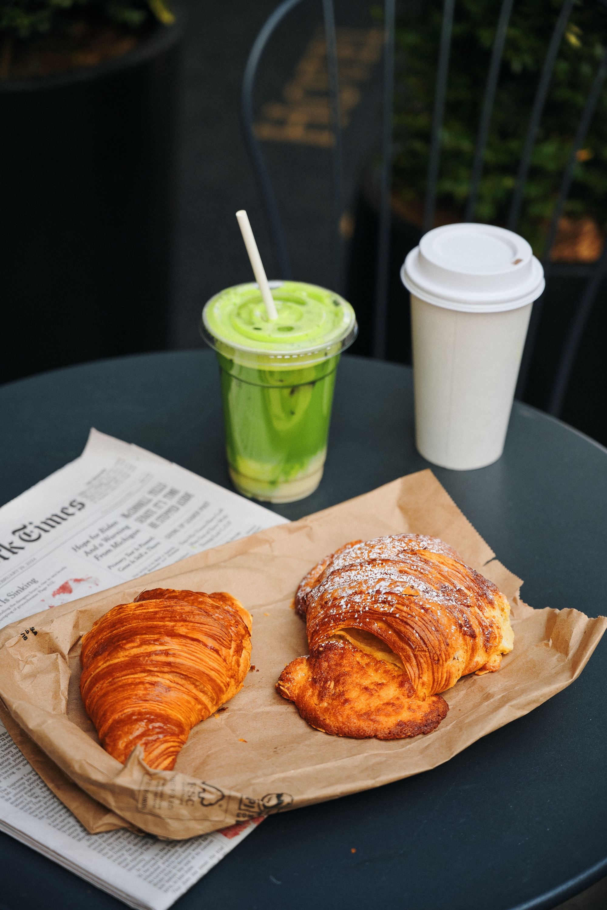 A table with two croissants, a coffee cup, and a green drink on it.