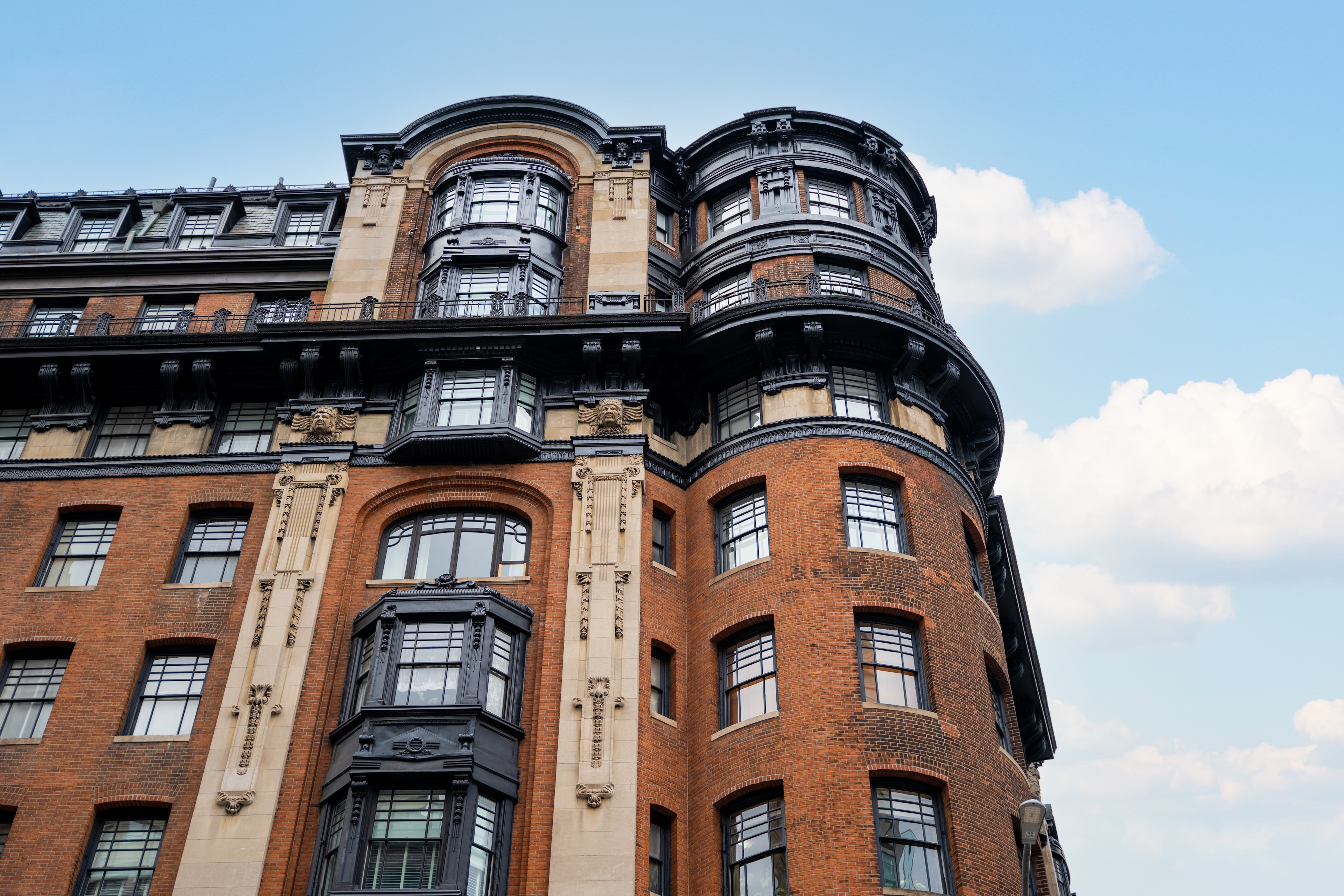 A red brick building with black and beige accents and balconies under a blue sky with clouds.