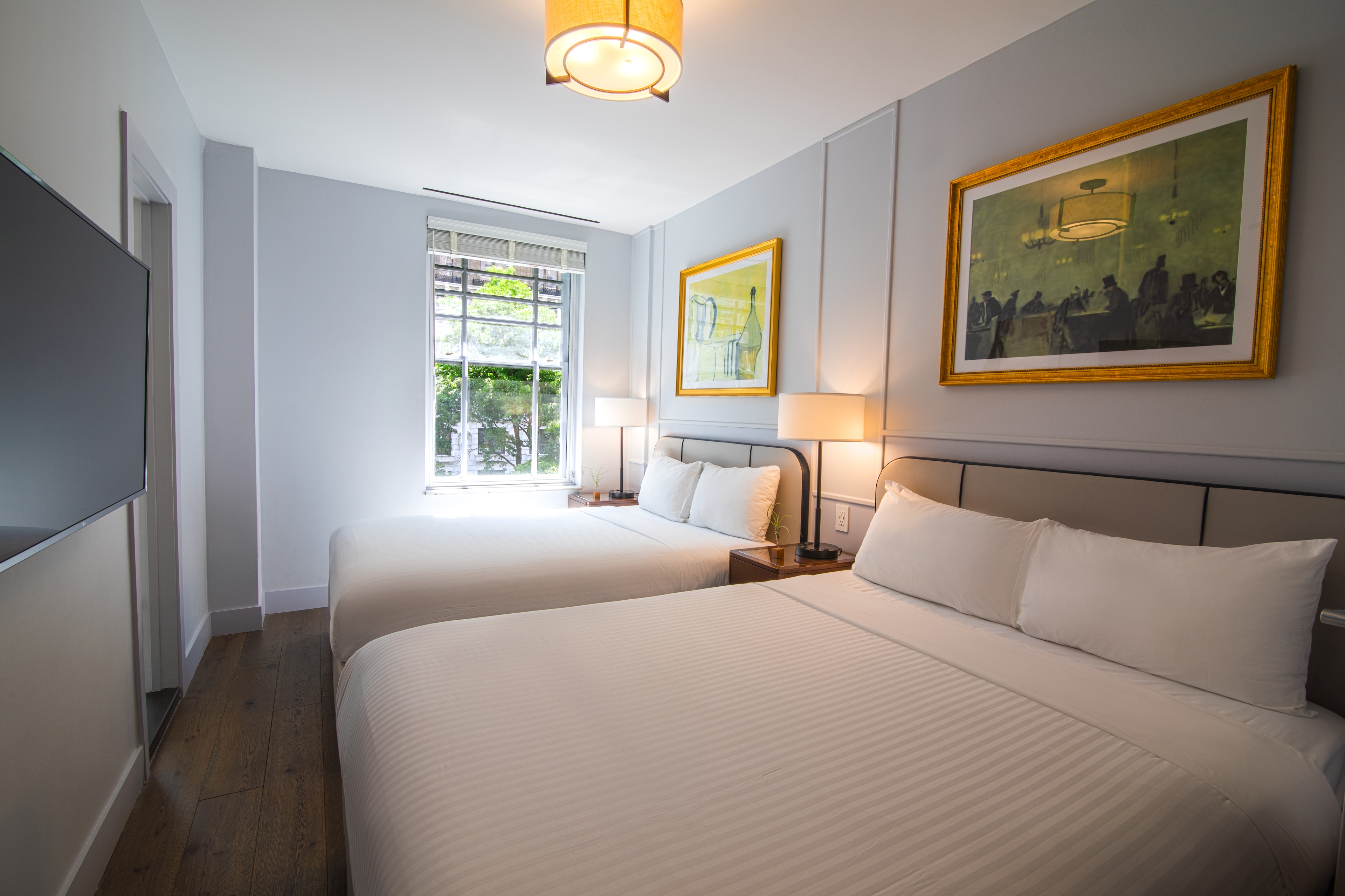 A wide view of a hotel room with two beds, a window, and artwork on the walls.