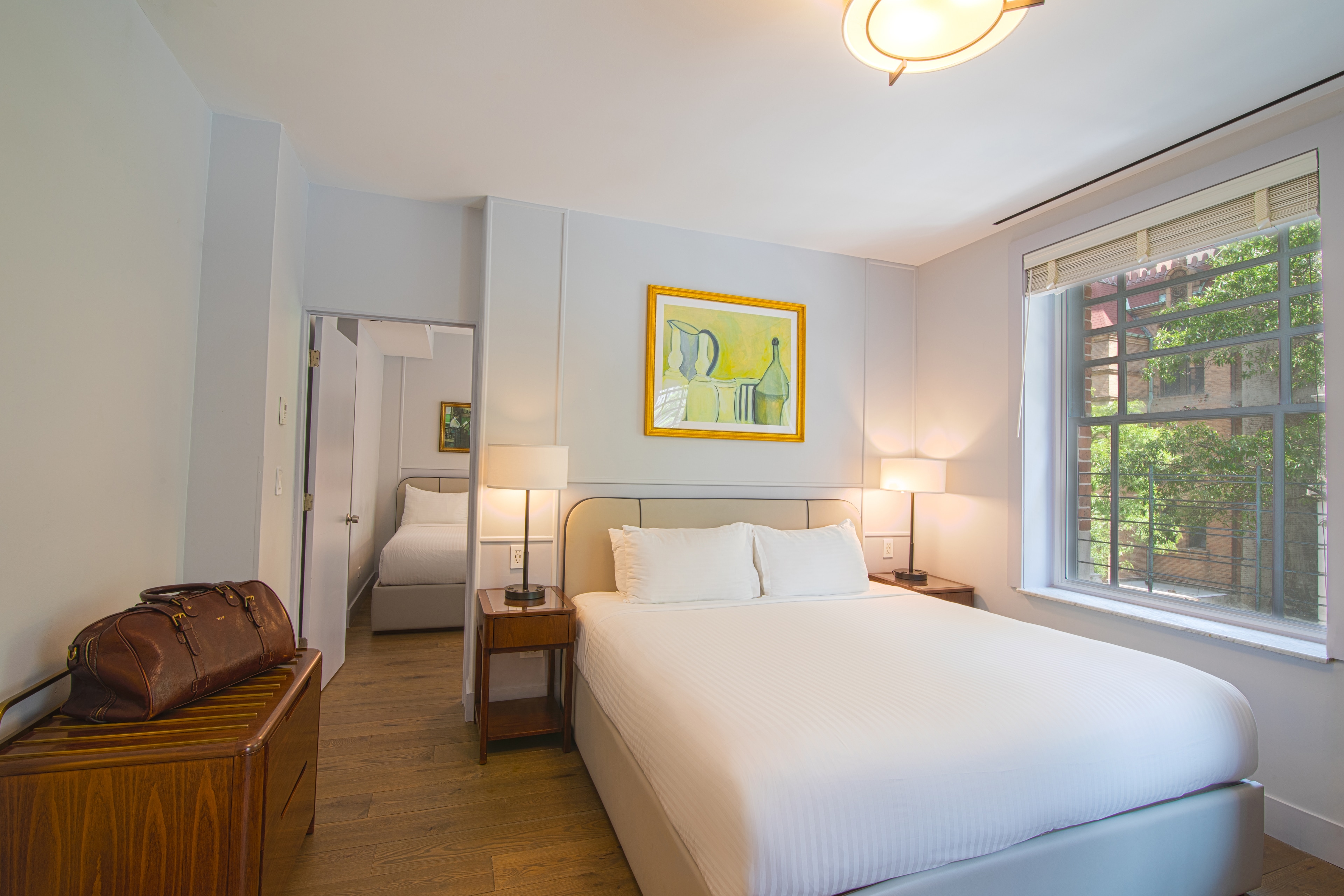 A hotel room with a large bed, two nightstands, a window, and a doorway to another room.