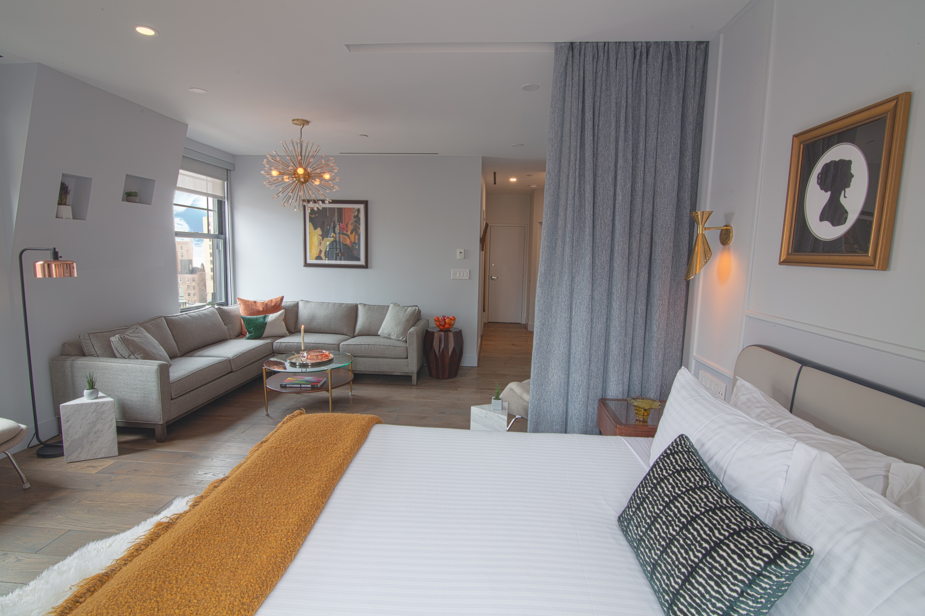 A spacious hotel room with a large bed, sofa, coffee table, and window