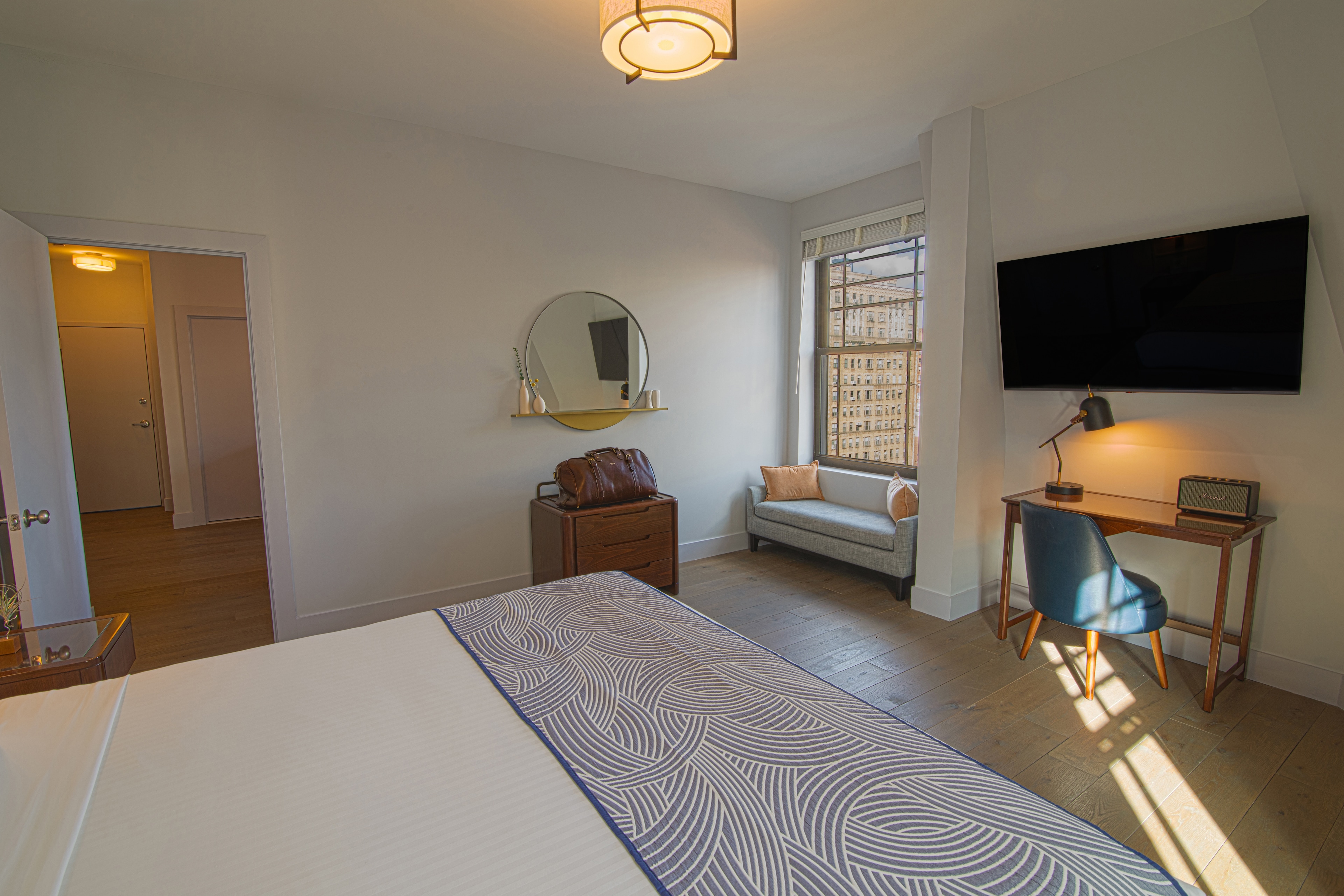 A hotel room with a bed, desk, TV, and window