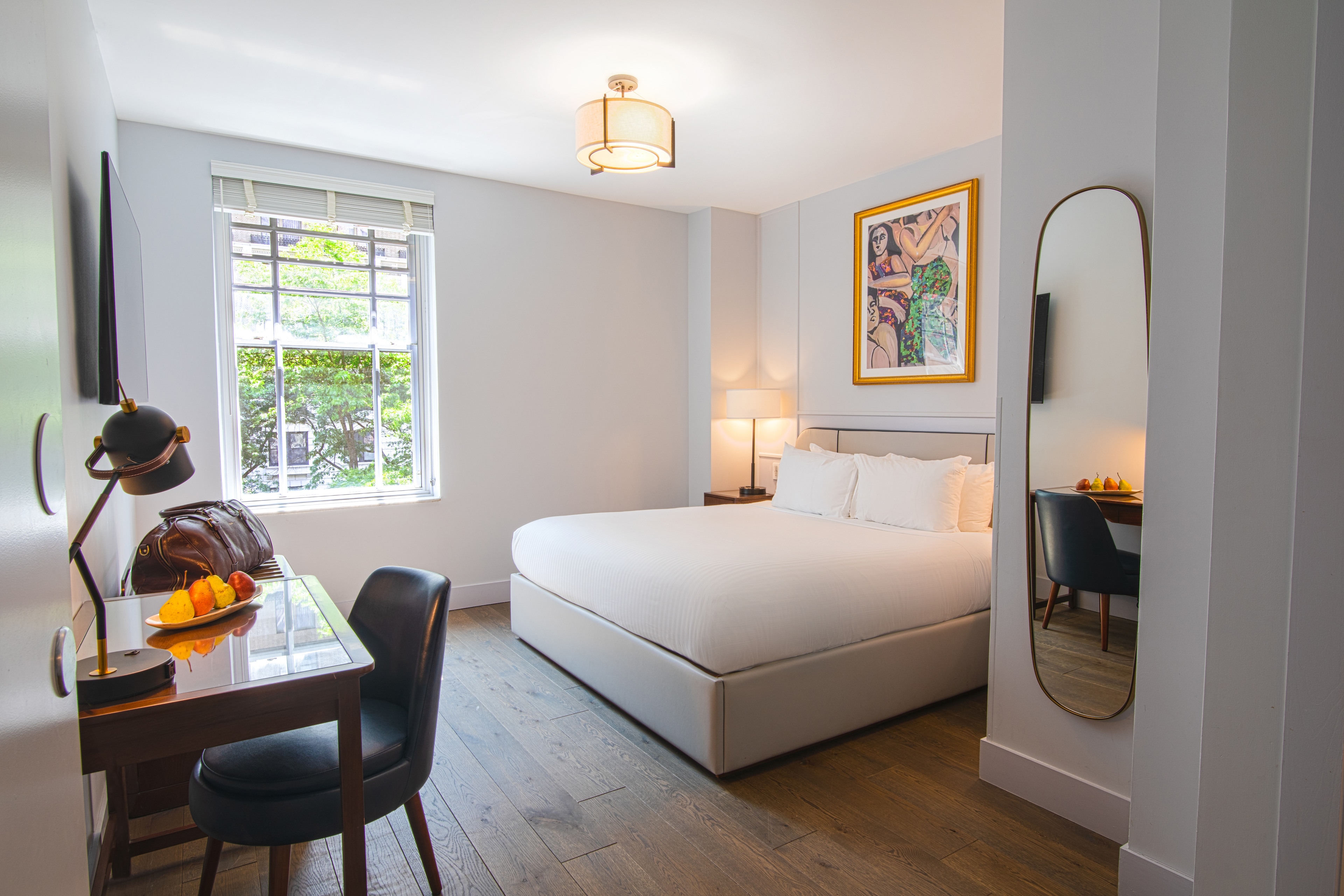 A hotel room with a large bed, window, desk, and mirror