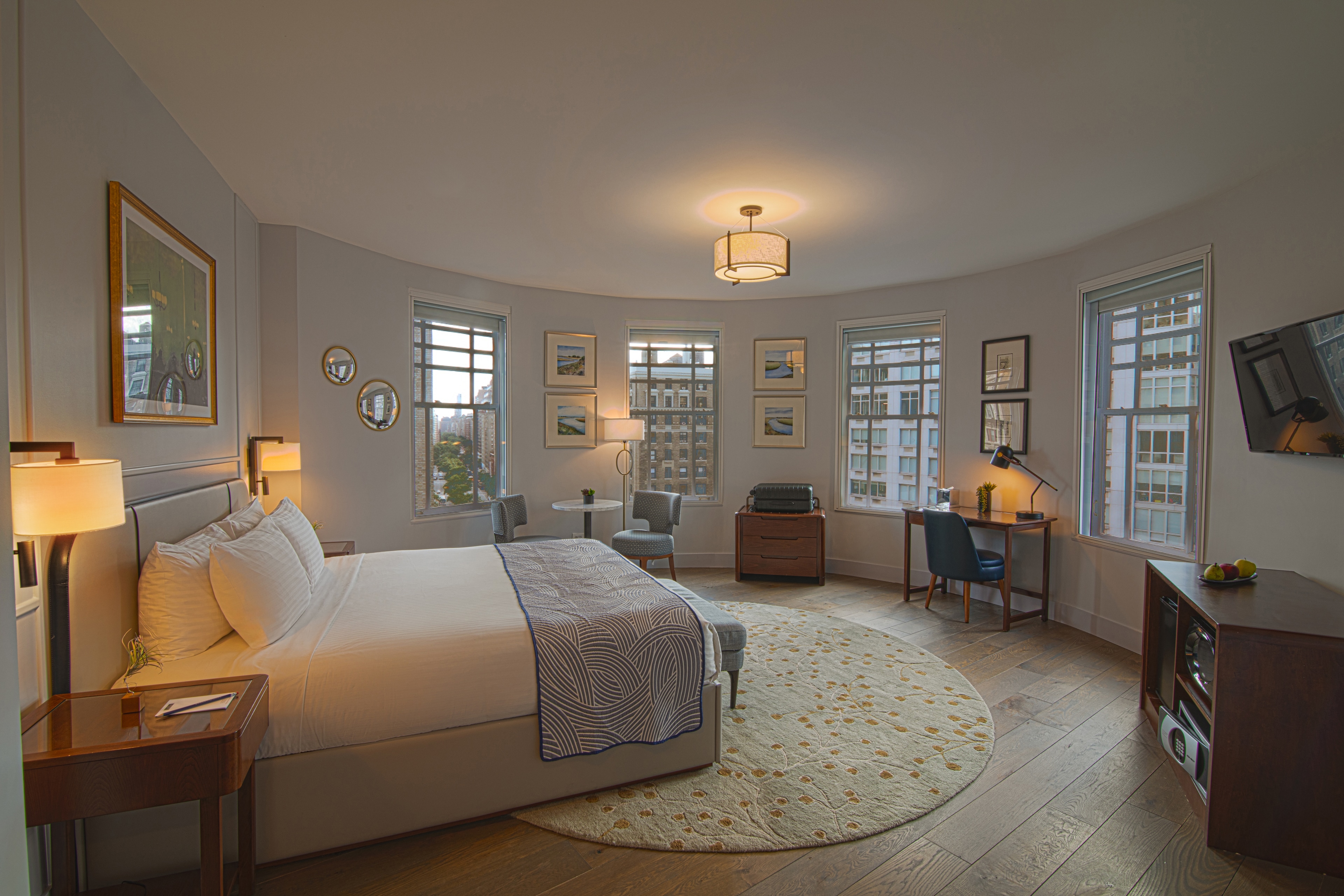 A wide view of a spacious hotel room with a large bed, desk, chair, and windows.