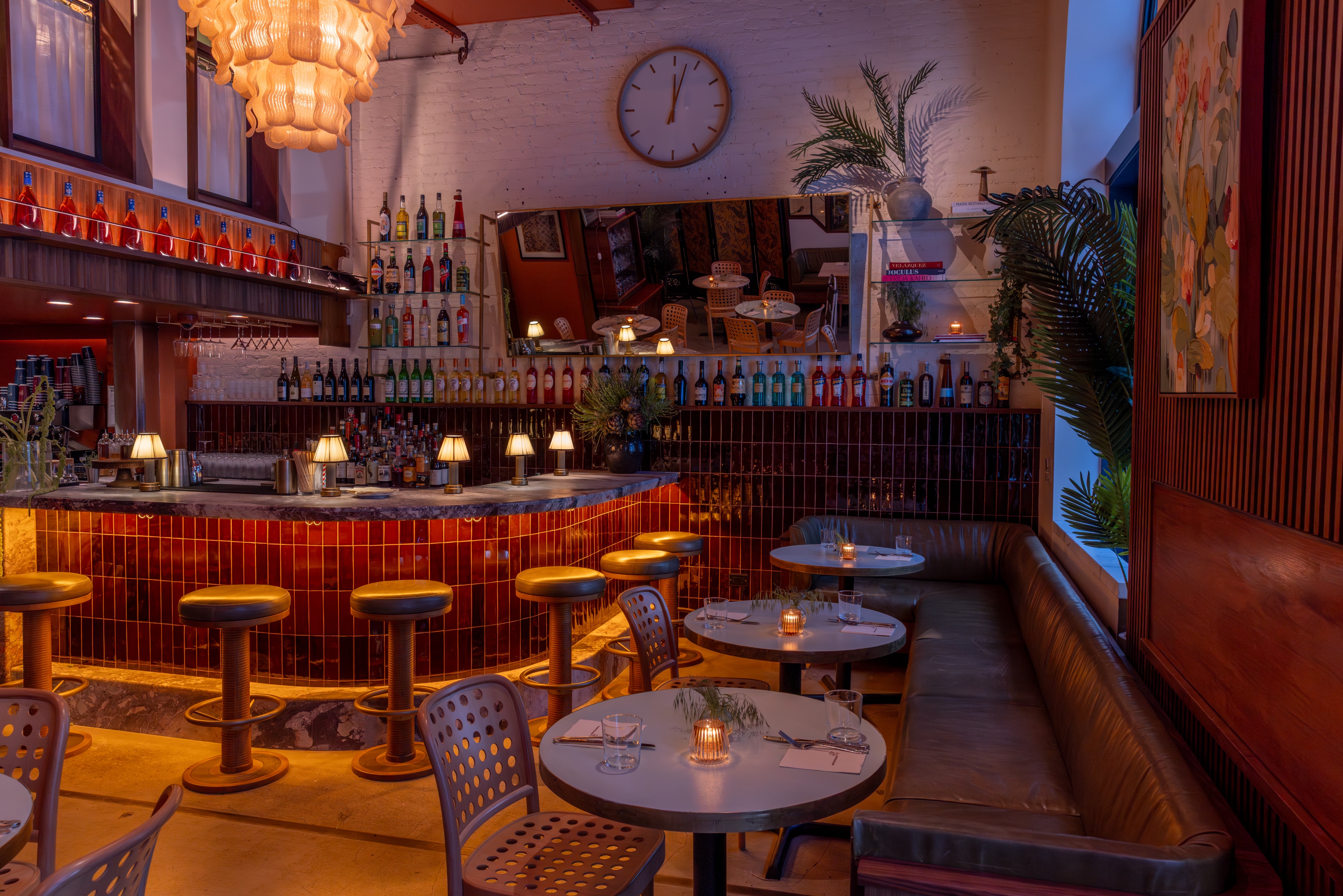 A dimly lit bar with a red tiled counter, seating area, and tables set for dining.