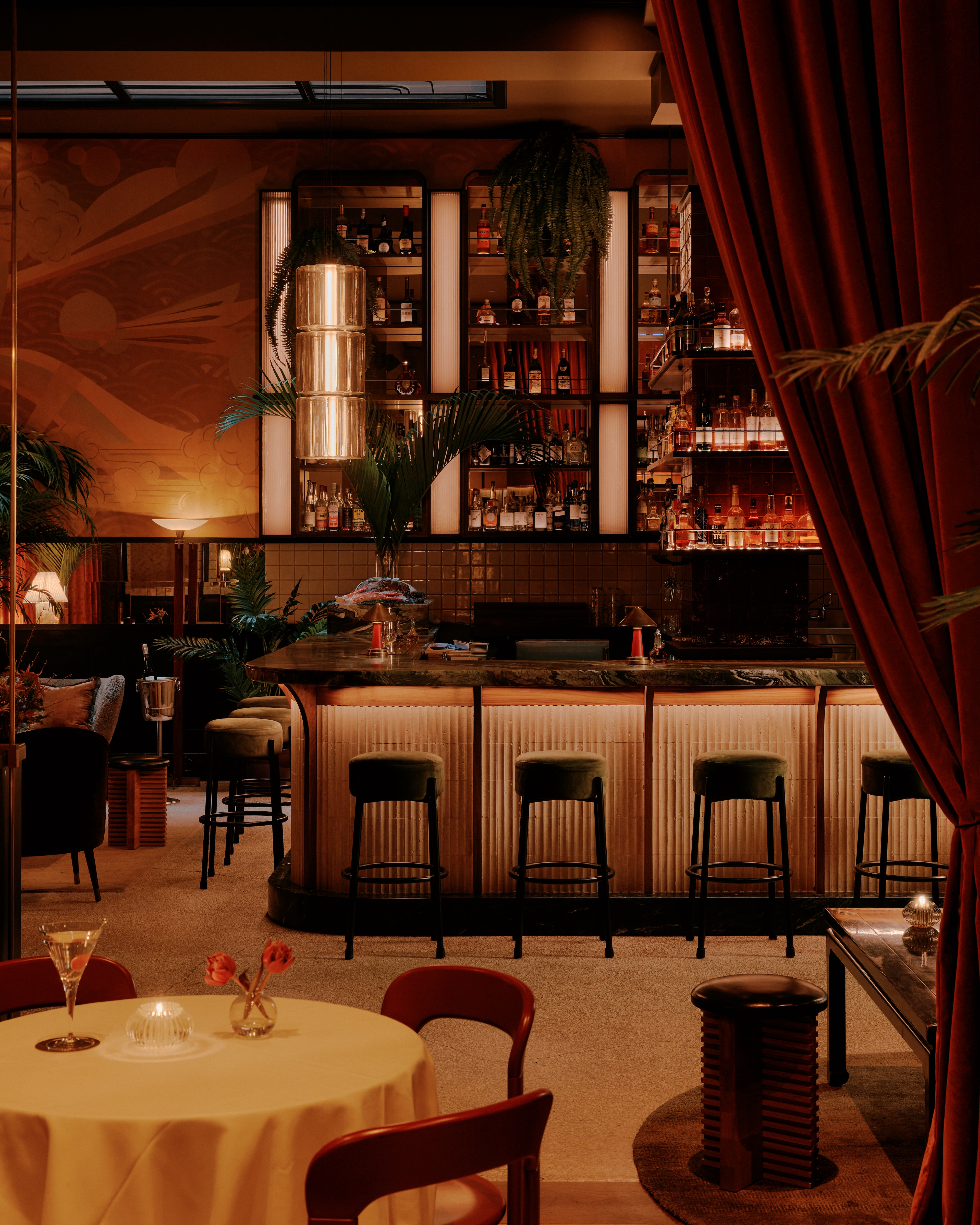 A dimly lit bar with a marble counter, barstools, and a few tables with chairs.