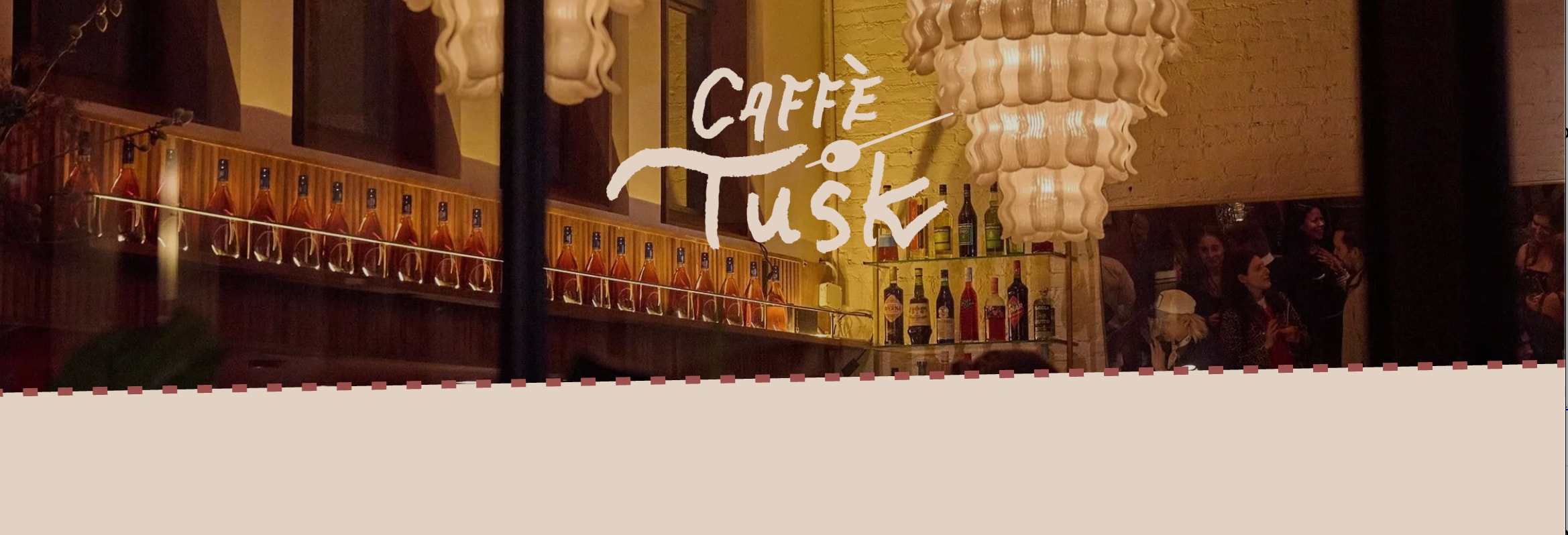 A dimly lit bar with a chandelier, bottles on shelves, and people in the background.