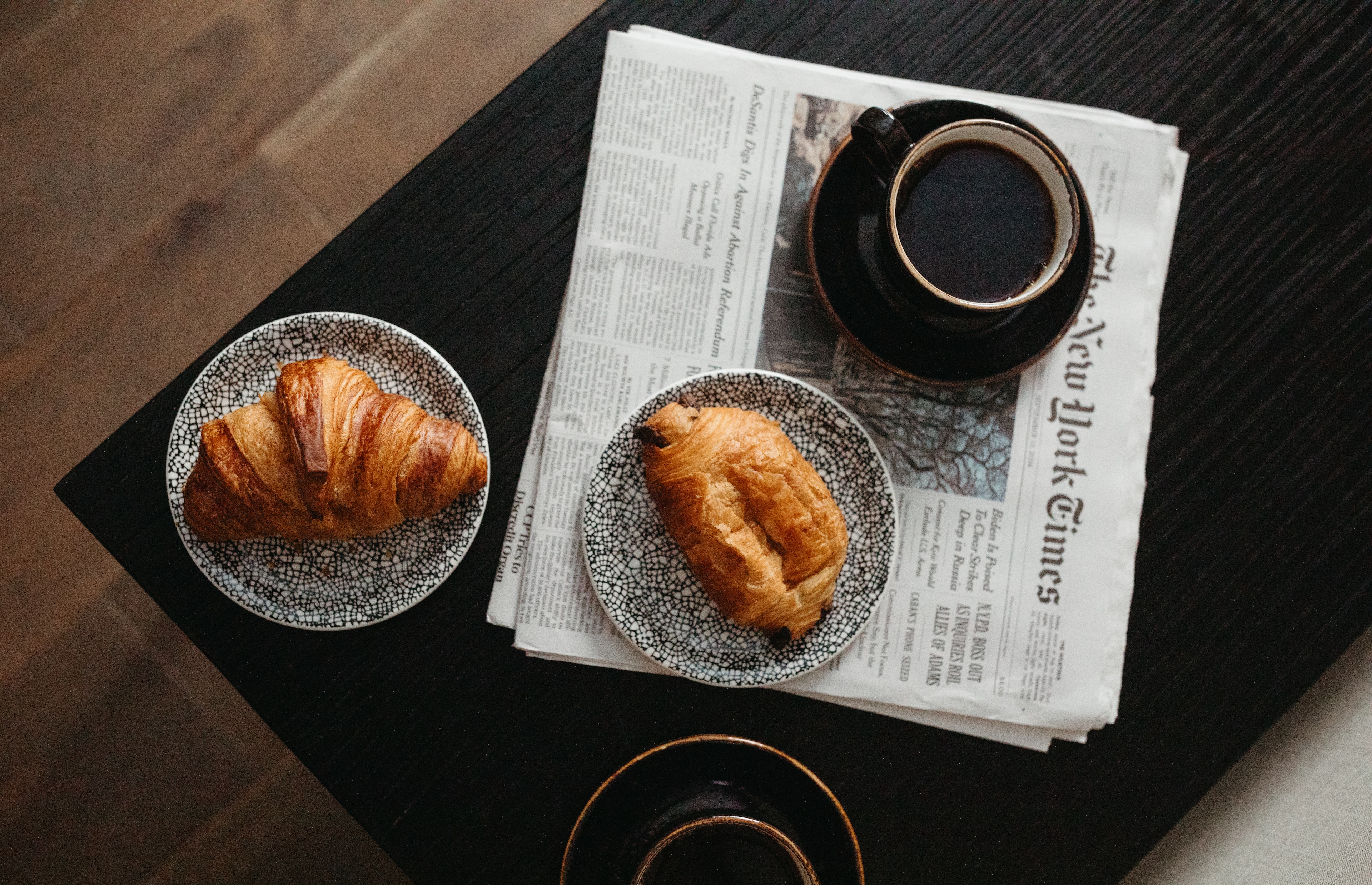 A breakfast setup with croissants, coffee, and a newspaper on a table.
