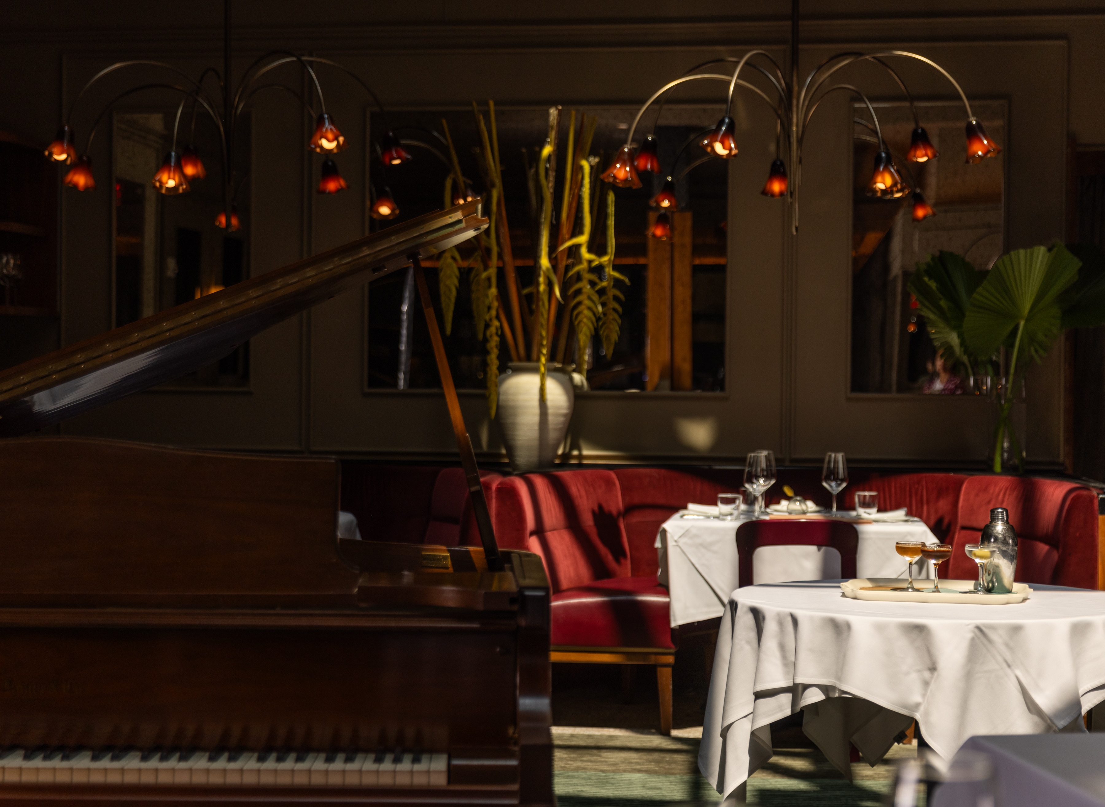 A dimly lit lounge with a grand piano, red couches, and white tablecloths.